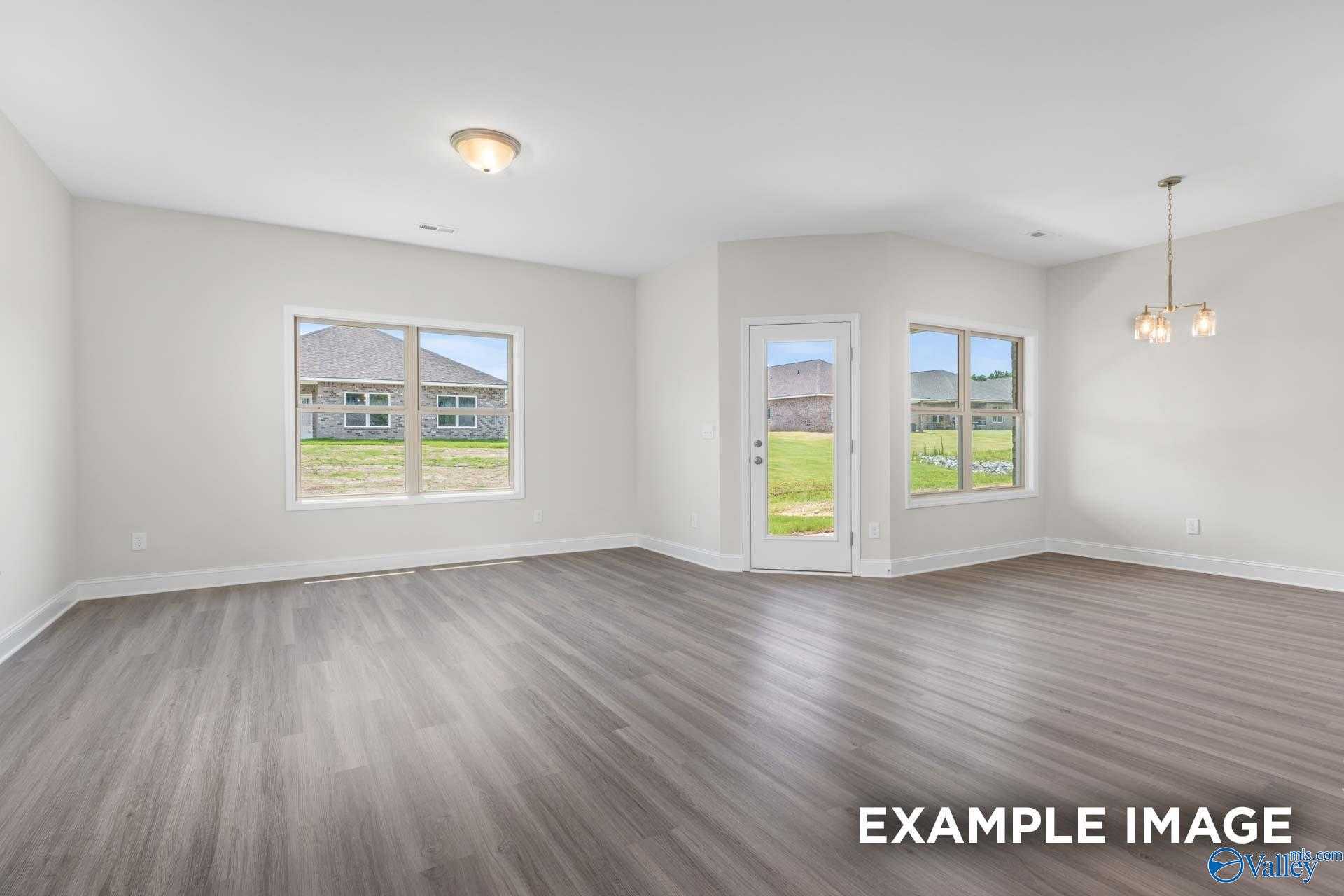 Bright open living room with wood floors, large windows, and glass door to green lawn in Davidson Homes The Daphne D, Arab, Alabama