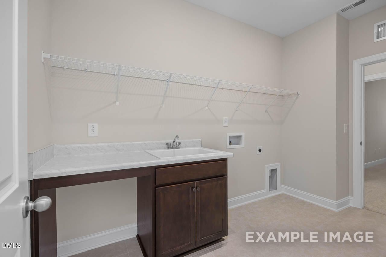 Modern laundry room with white quartz countertop, brown cabinets, deep sink, and drying rod in 4-bedroom Davidson Homes Crawford D, Angier, NC
