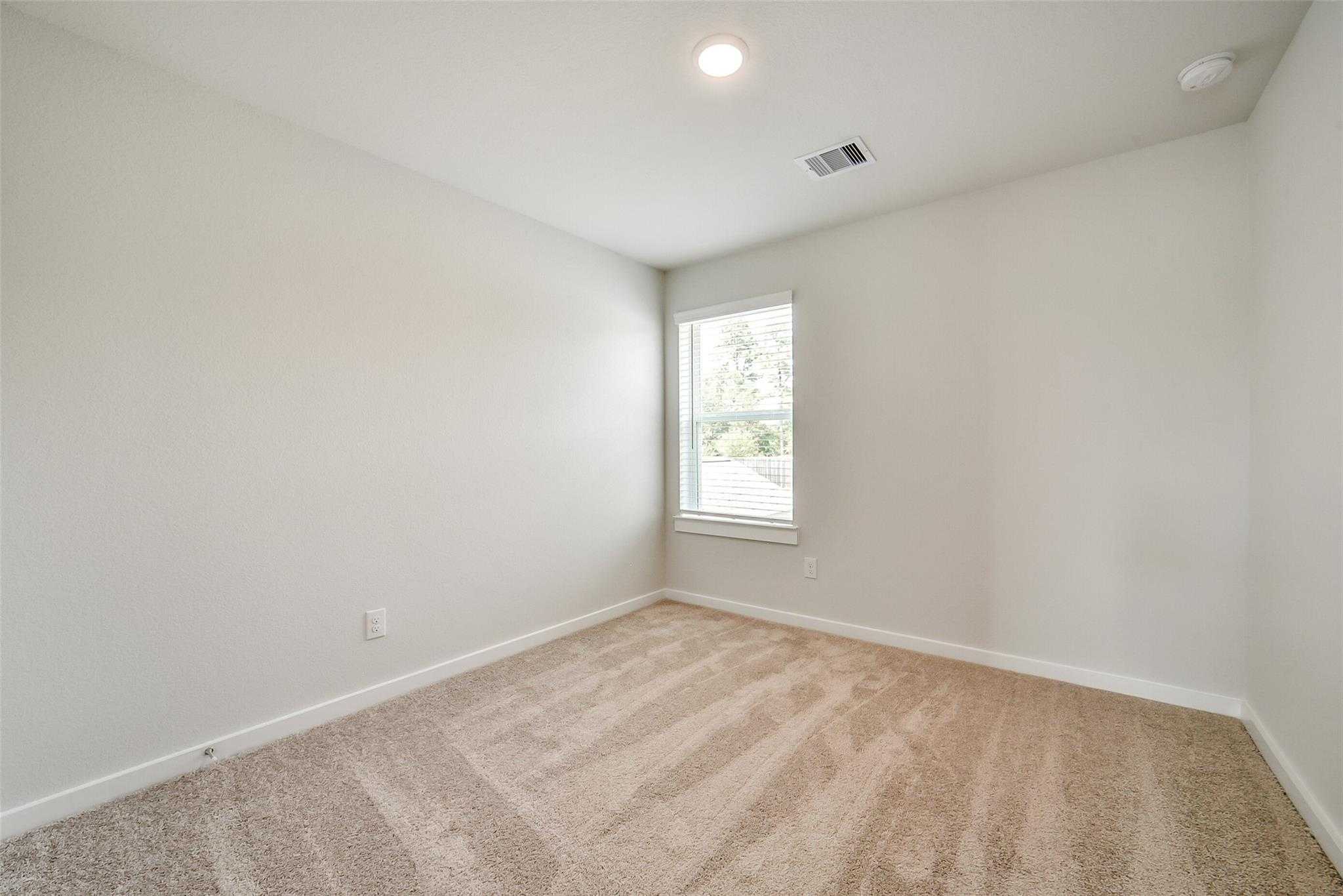 Bright secondary bedroom with neutral beige walls, tan carpet, and large window in Davidson Homes The Blanco E, Magnolia TX