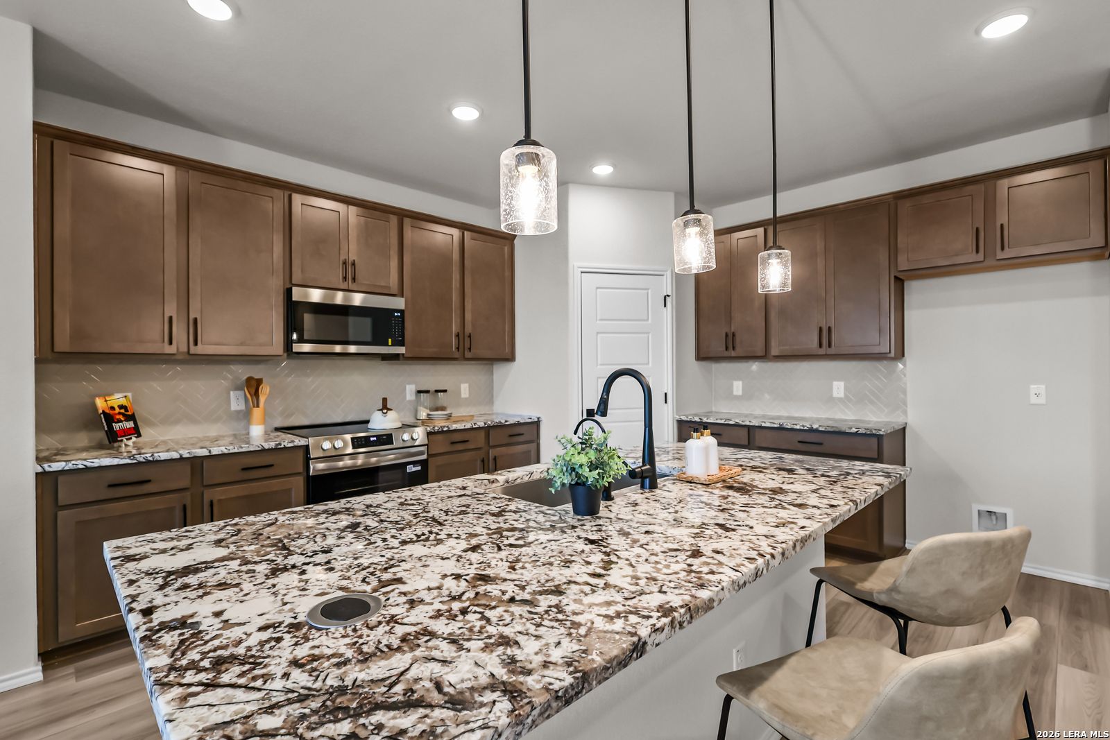 Modern kitchen with granite island and dark wood cabinets in The Douglas C floor plan at Hannah Heights in Seguin, Texas.
