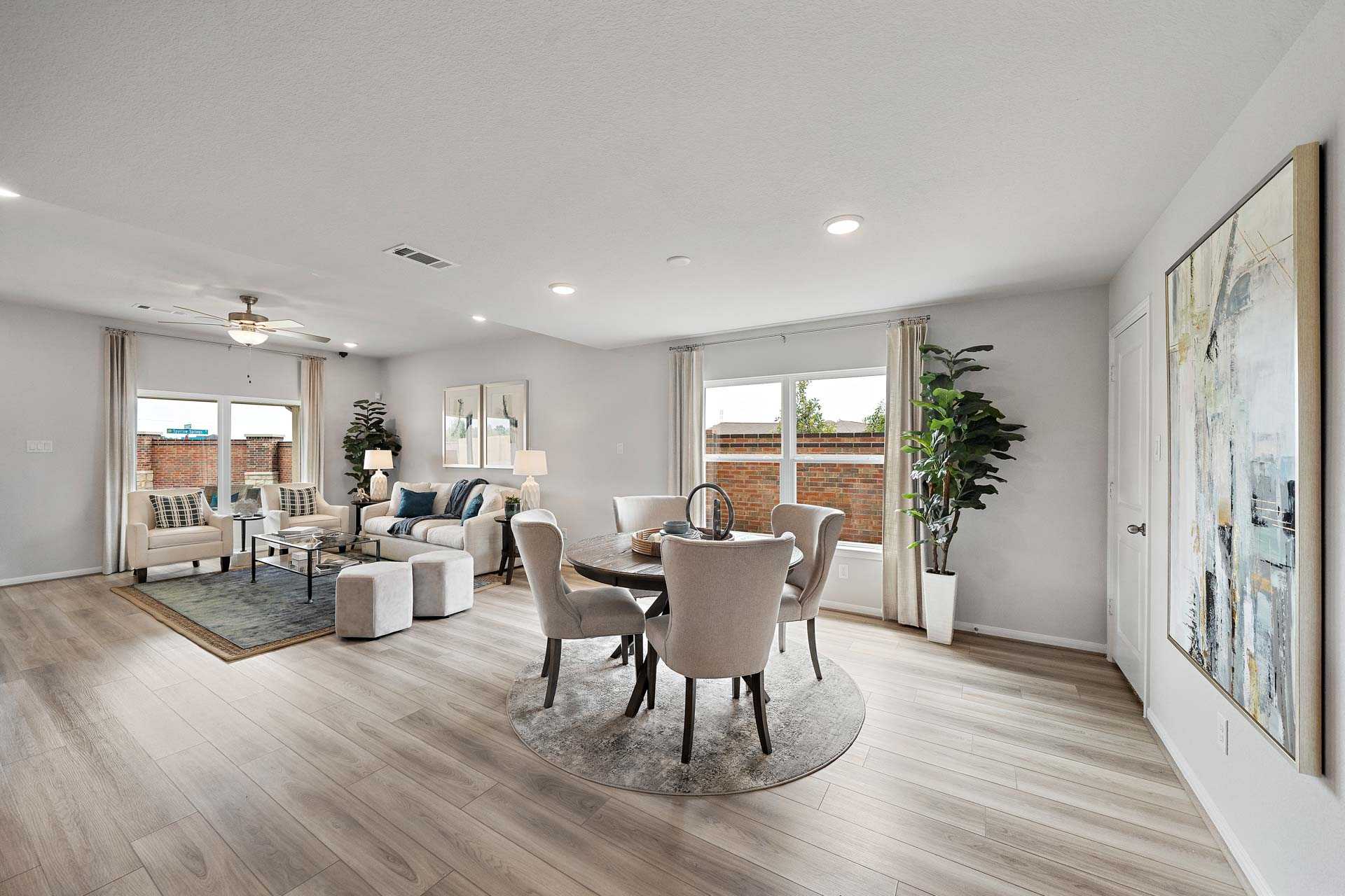 Open-concept living and dining room at Sunterra in Katy TX by Davidson Homes with light wood floors, beige furniture, large windows, and potted plants