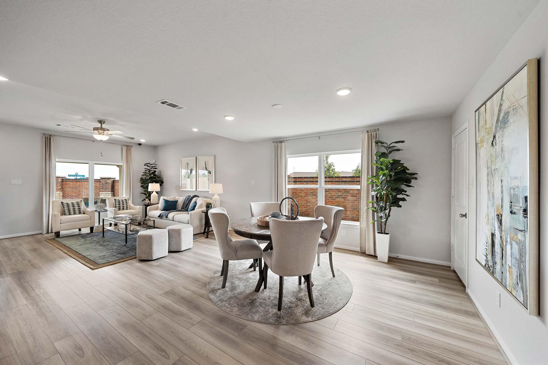 Open-concept living and dining room at Sunterra in Katy TX by Davidson Homes with light wood floors, beige furniture, large windows, and potted plants