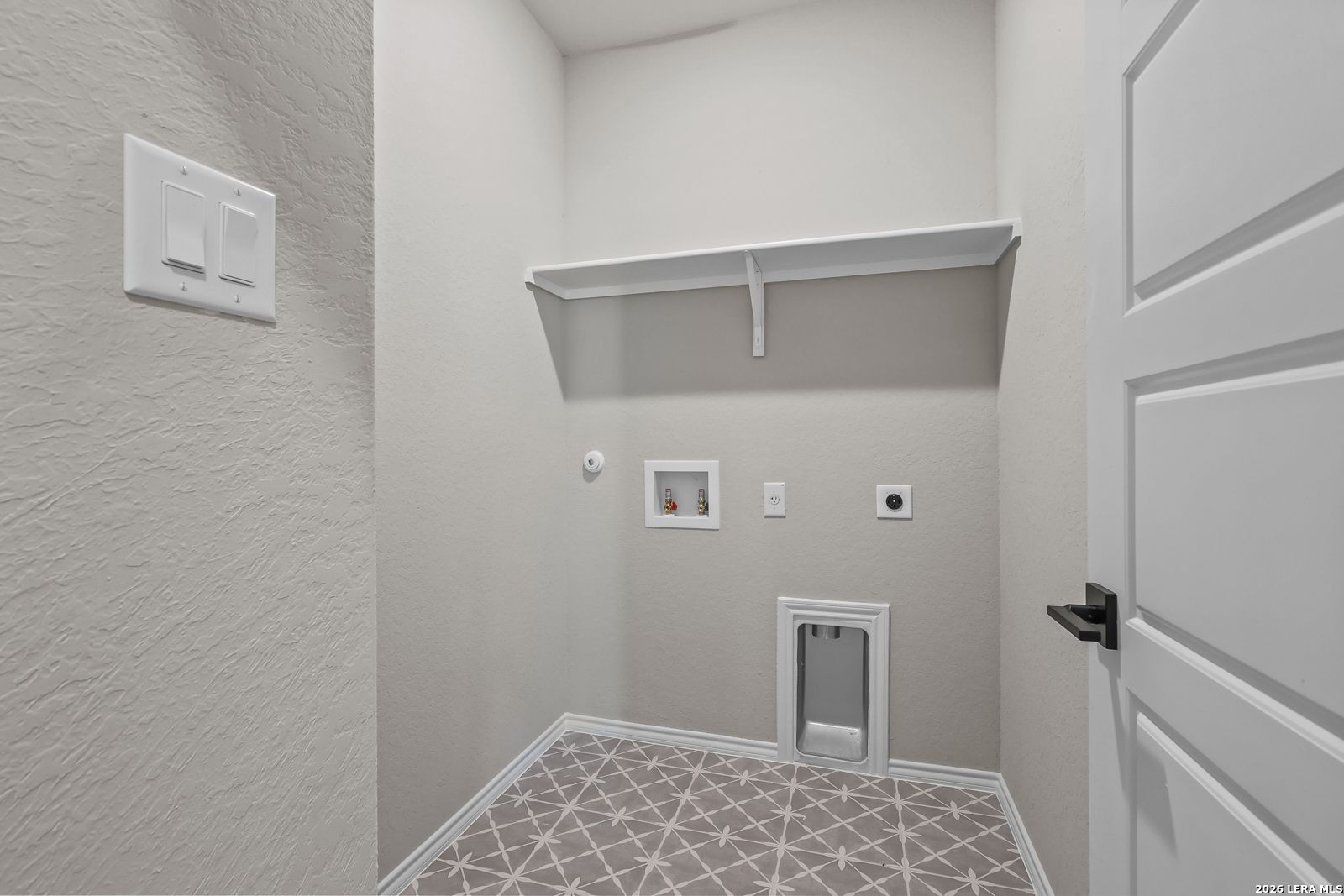 Dedicated laundry room with patterned tile flooring and storage shelf in The Daphne H floor plan, Hannah Heights, Seguin.