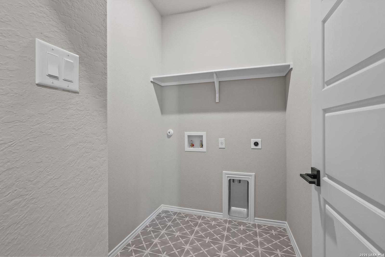 Dedicated laundry room with patterned tile flooring and storage shelf in The Daphne H floor plan, Hannah Heights, Seguin.