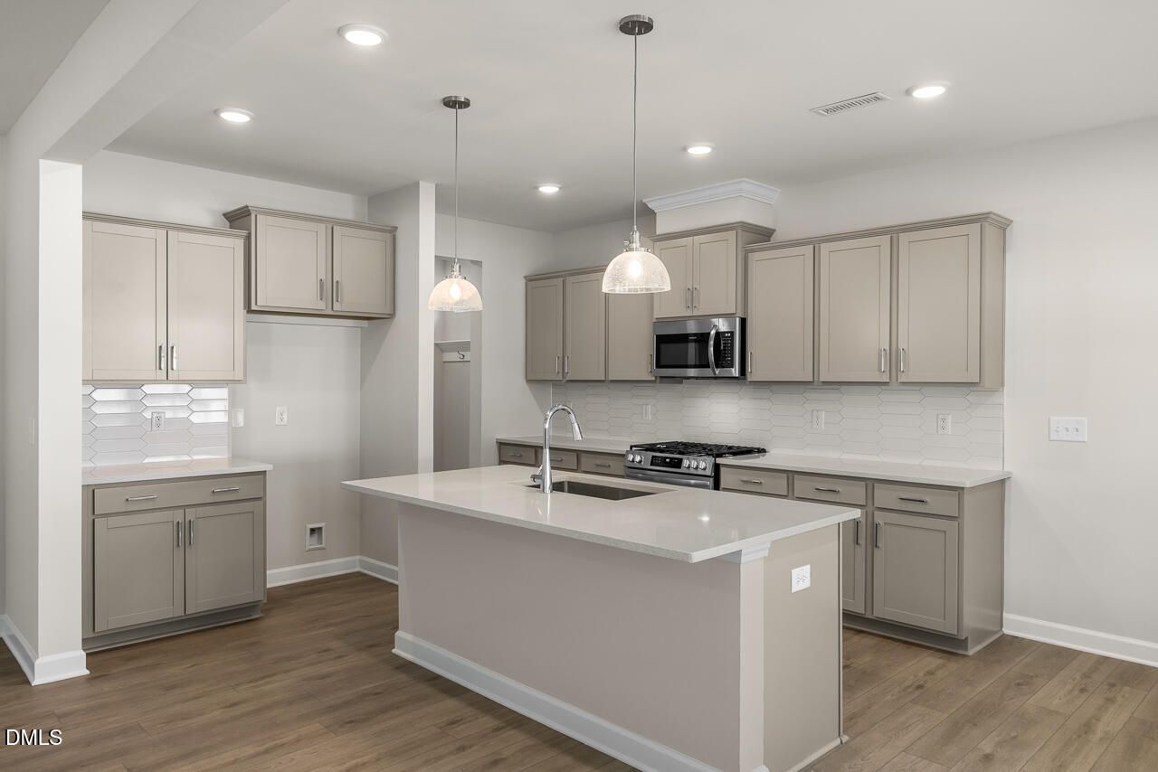 Modern kitchen with quartz island, gray cabinets, and tile backsplash in The Gavin A floor plan, Gregory Village, Lillington.