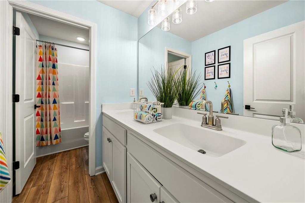 Bright kids' bathroom with light blue walls, colorful geometric shower curtain, white vanity sink in Davidson Homes The Hickory B, Riverwood, Dallas, Georgia