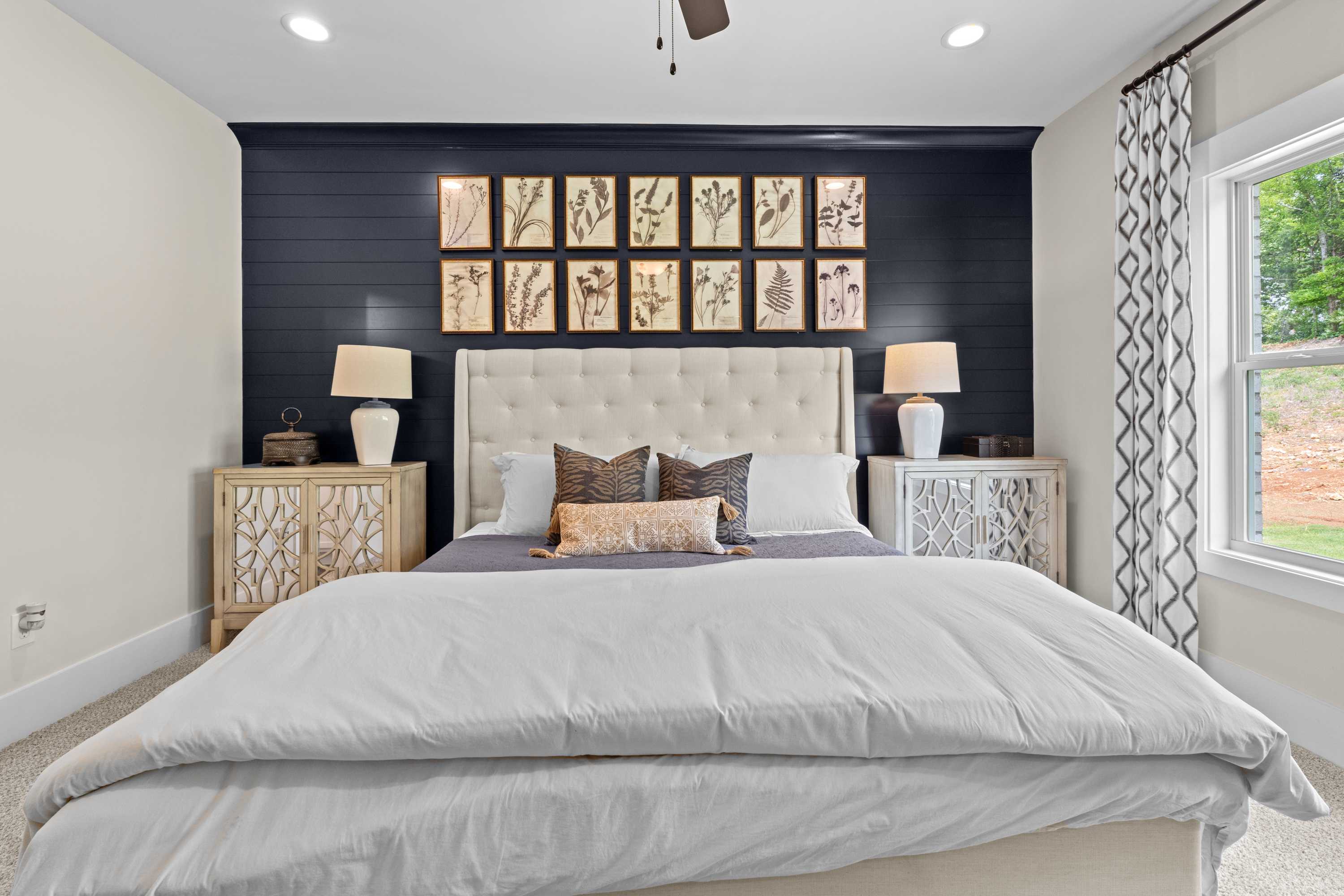 Spacious master bedroom at Ivy Hills in Toney Alabama by Davidson Homes with tufted beige headboard navy shiplap wall botanical prints and ceiling fan