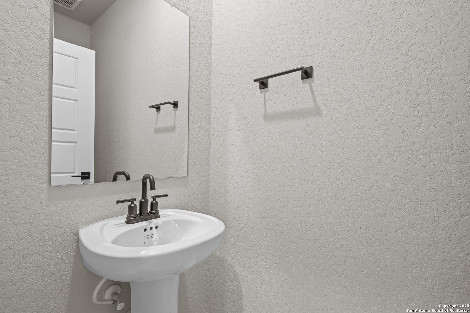 Elegant powder room with white pedestal sink, framed mirror, and towel bar in Davidson Homes The Murray J, San Antonio