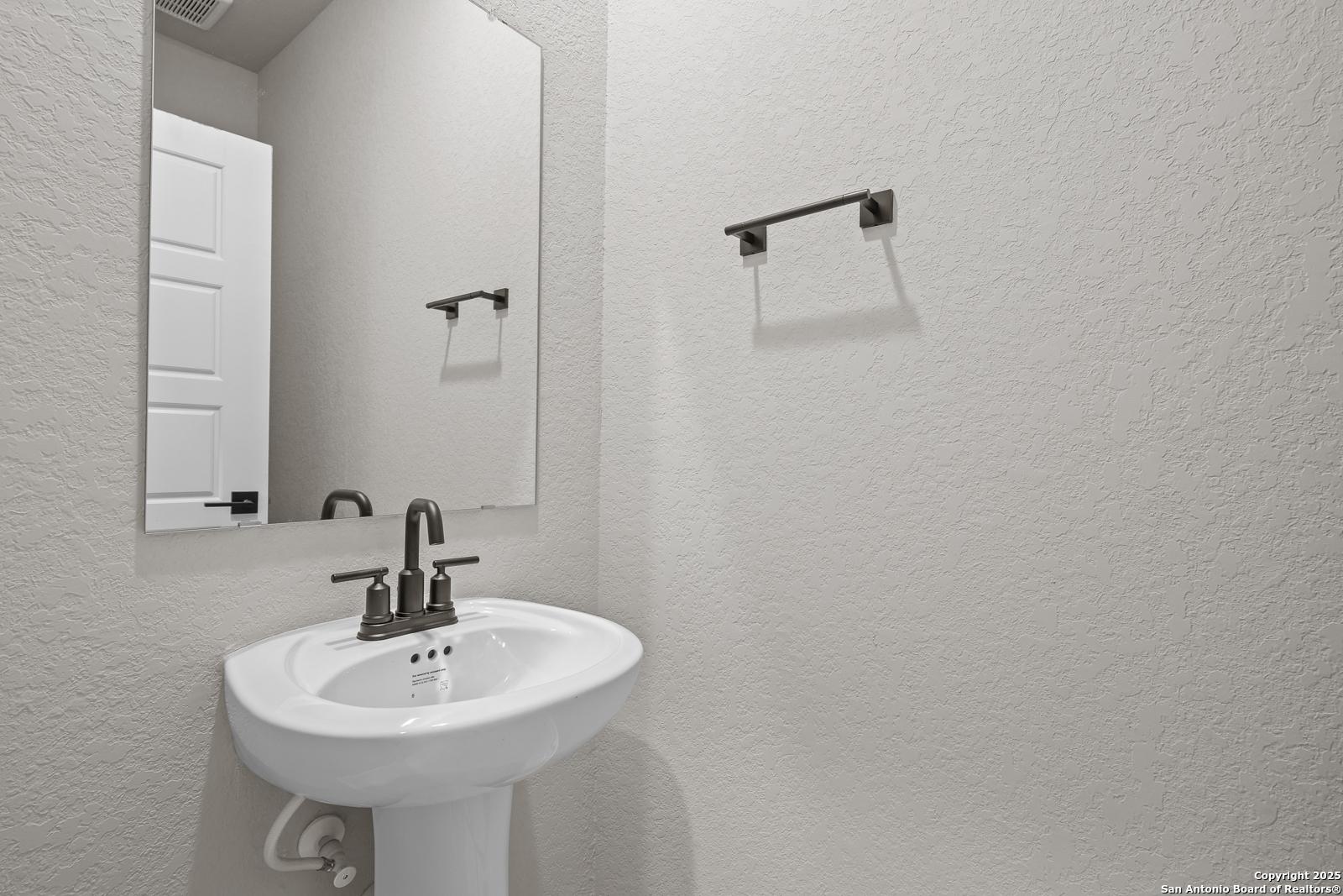 Elegant powder room with white pedestal sink, framed mirror, and towel bar in Davidson Homes The Murray J, San Antonio