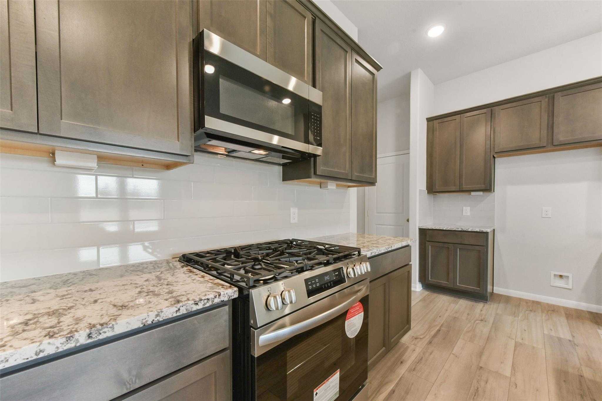Modern kitchen featuring stainless steel appliances, granite countertops, subway tile backsplash in Davidson Homes The Laguna B, Magnolia, Texas