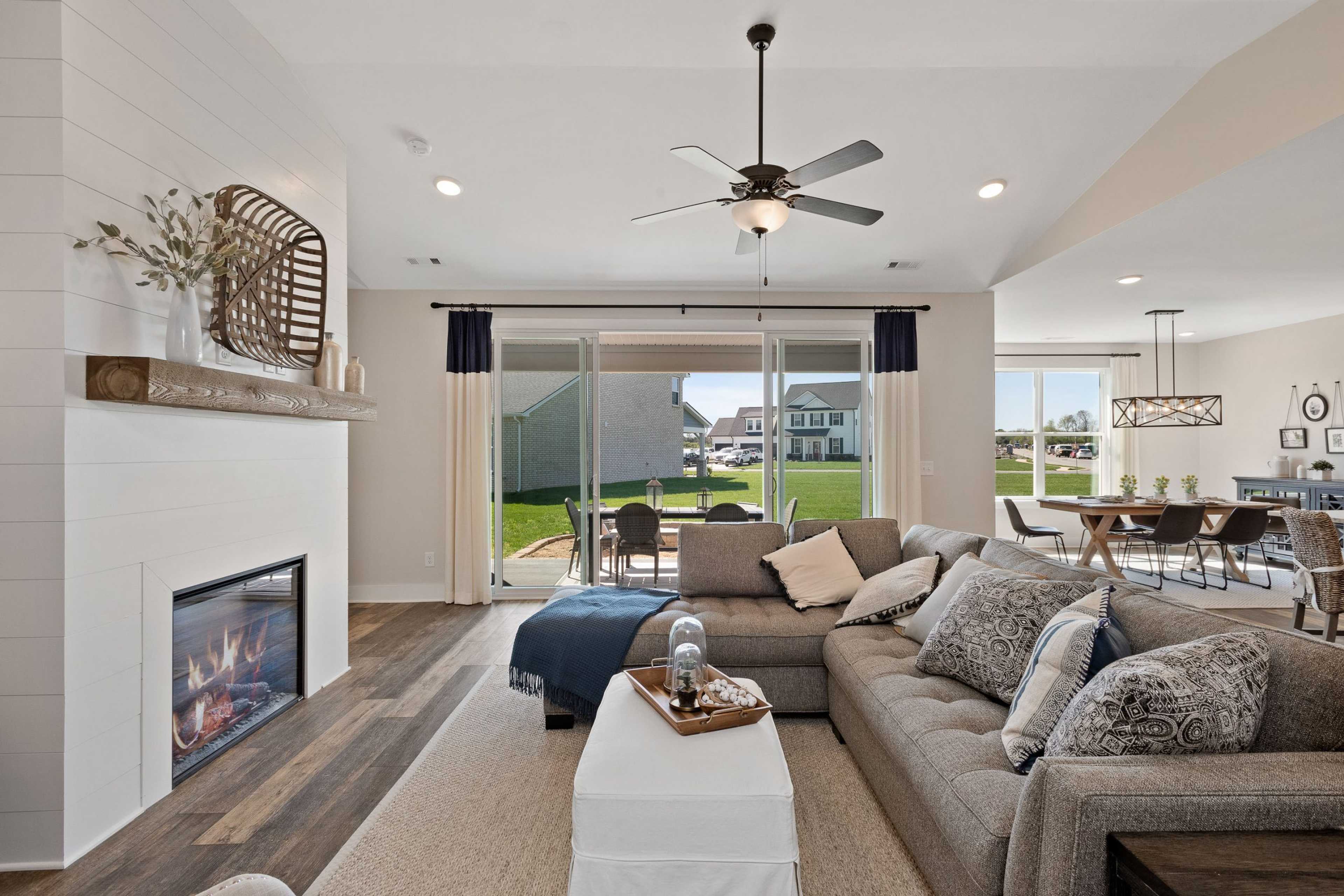 Open-concept living room at Rivers Edge in Murfreesboro TN featuring shiplap fireplace, gray sectional sofa, and sliding doors to backyard patio