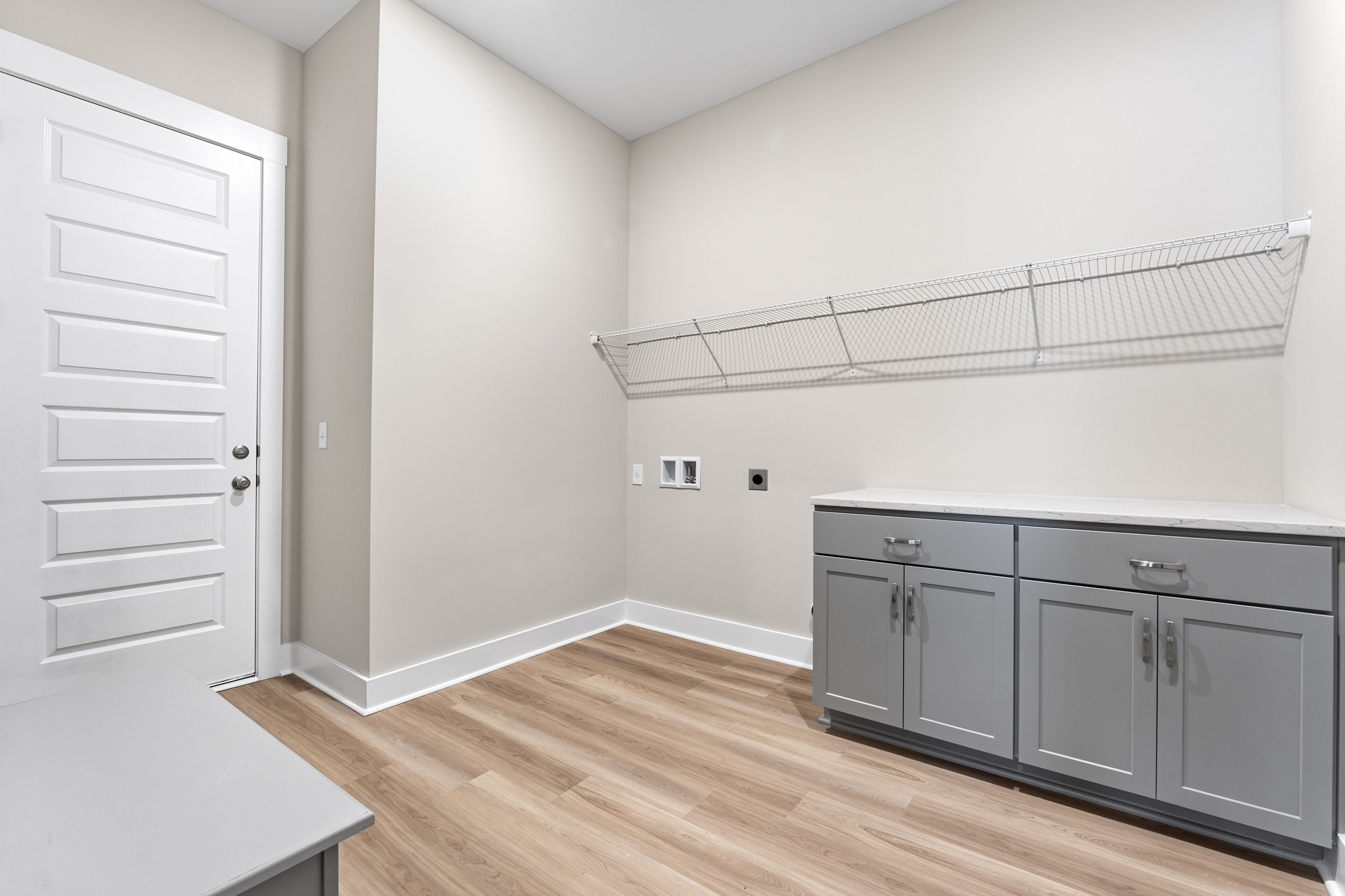 Spacious laundry room in The Oxford A with gray cabinets, wire shelving, washer-dryer outlets, and hardwood floors