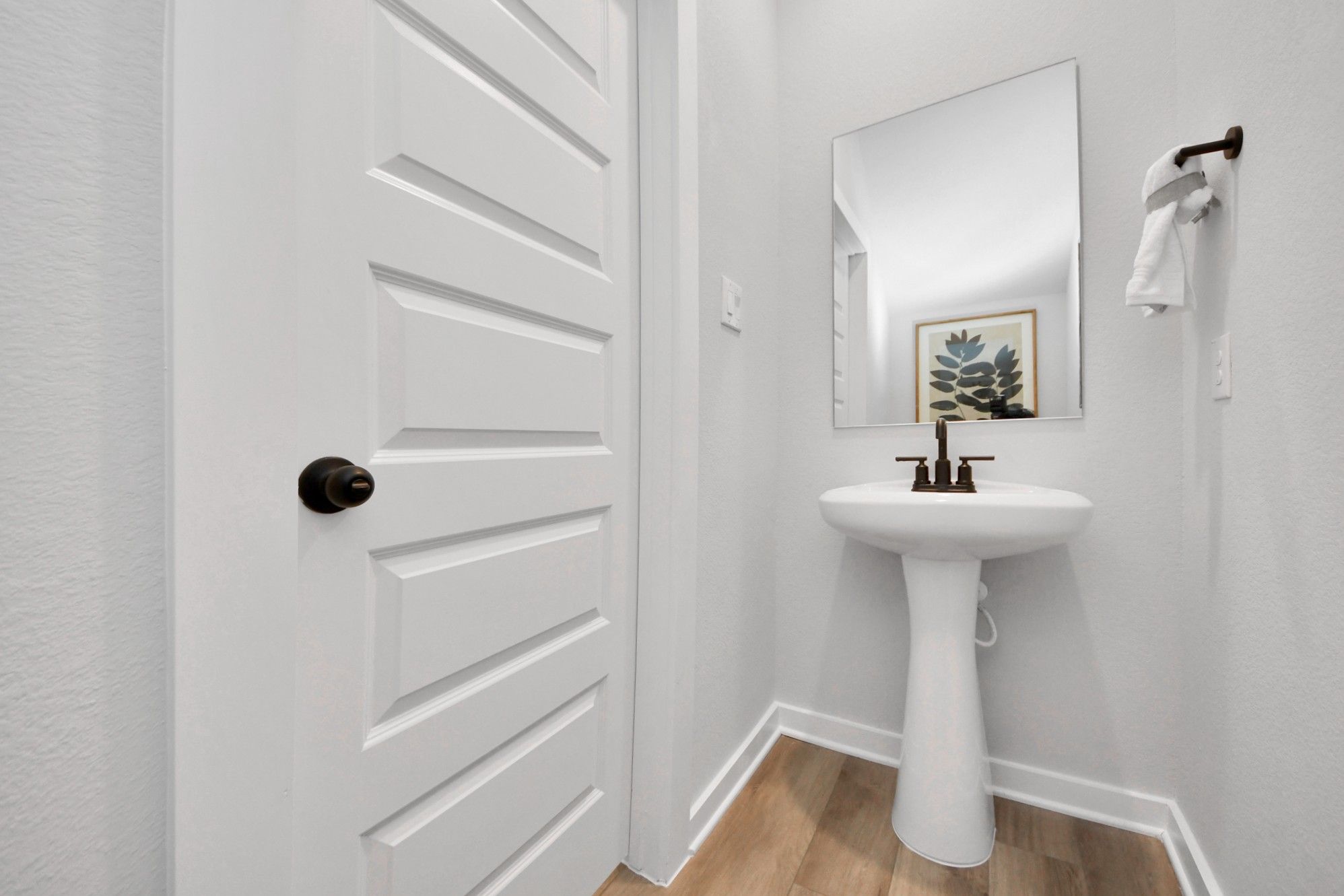 Modern powder room at Robins Landing in Houston, TX with a pedestal sink, bronze fixtures, and hardwood-style flooring.