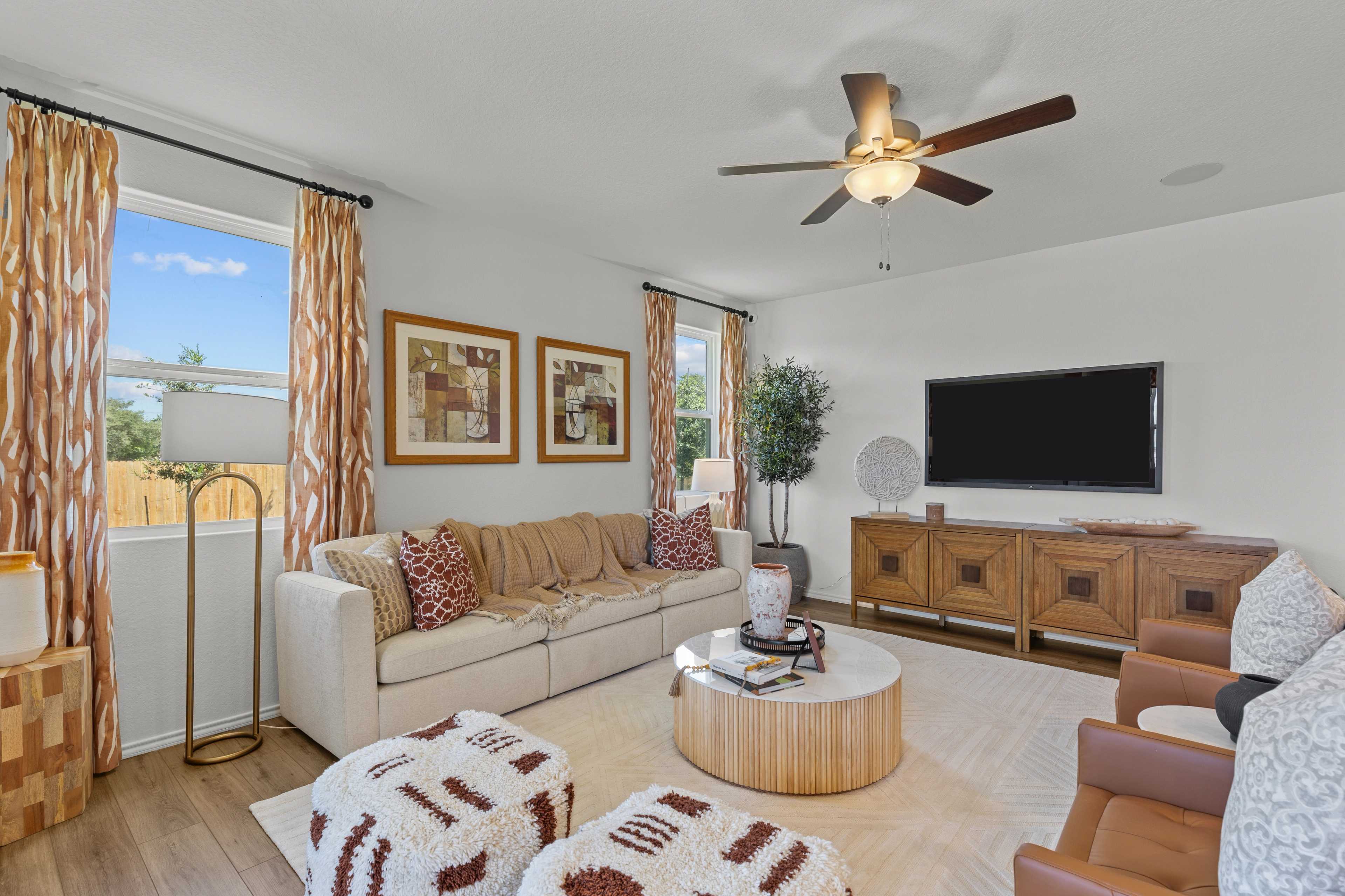 Cozy living room at Royal Crest in San Antonio Texas featuring beige sofa, wooden media console, TV, and large windows with patterned curtains