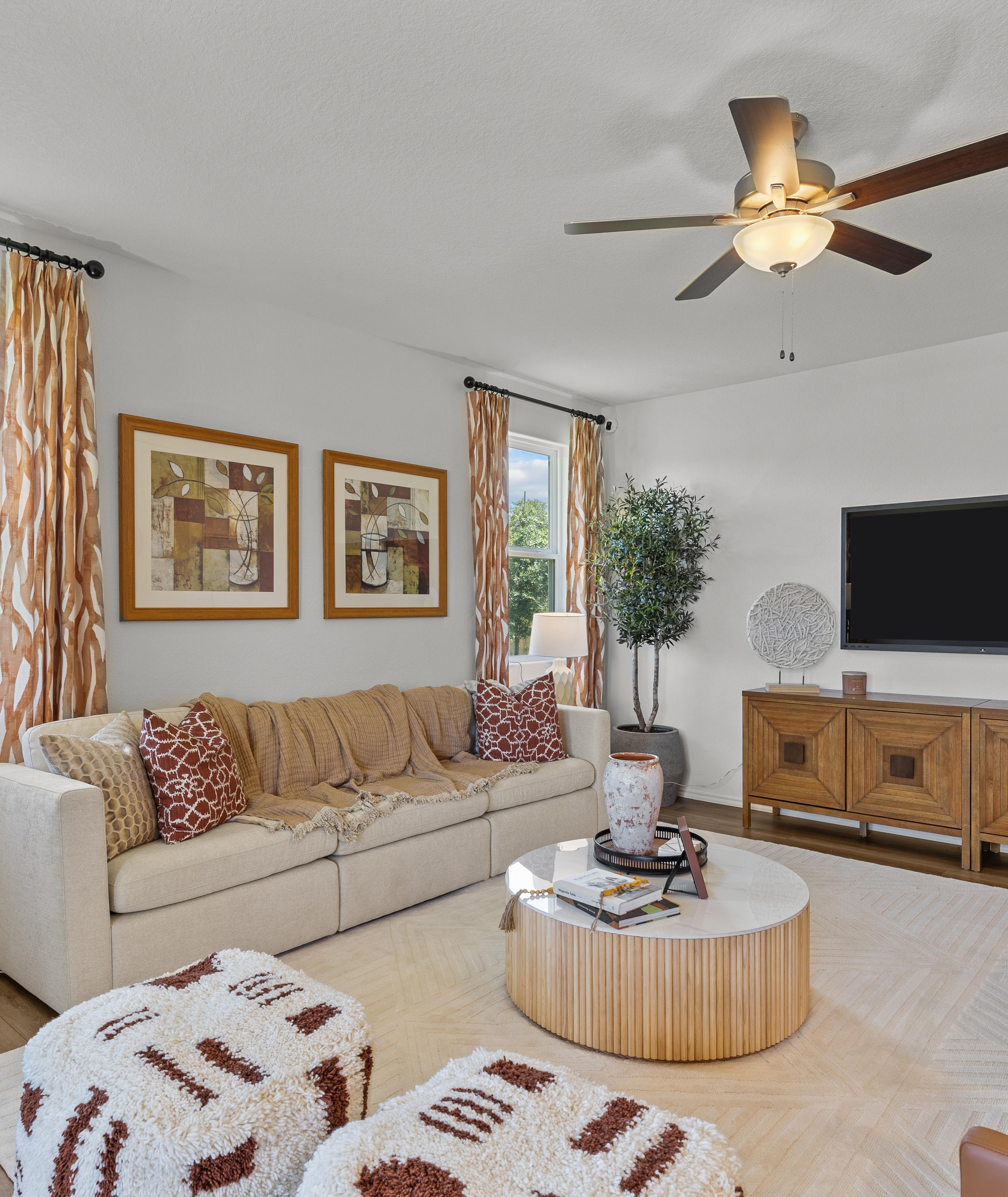 Cozy living room at Royal Crest in San Antonio Texas featuring beige sofa, wooden media console, TV, and large windows with patterned curtains
