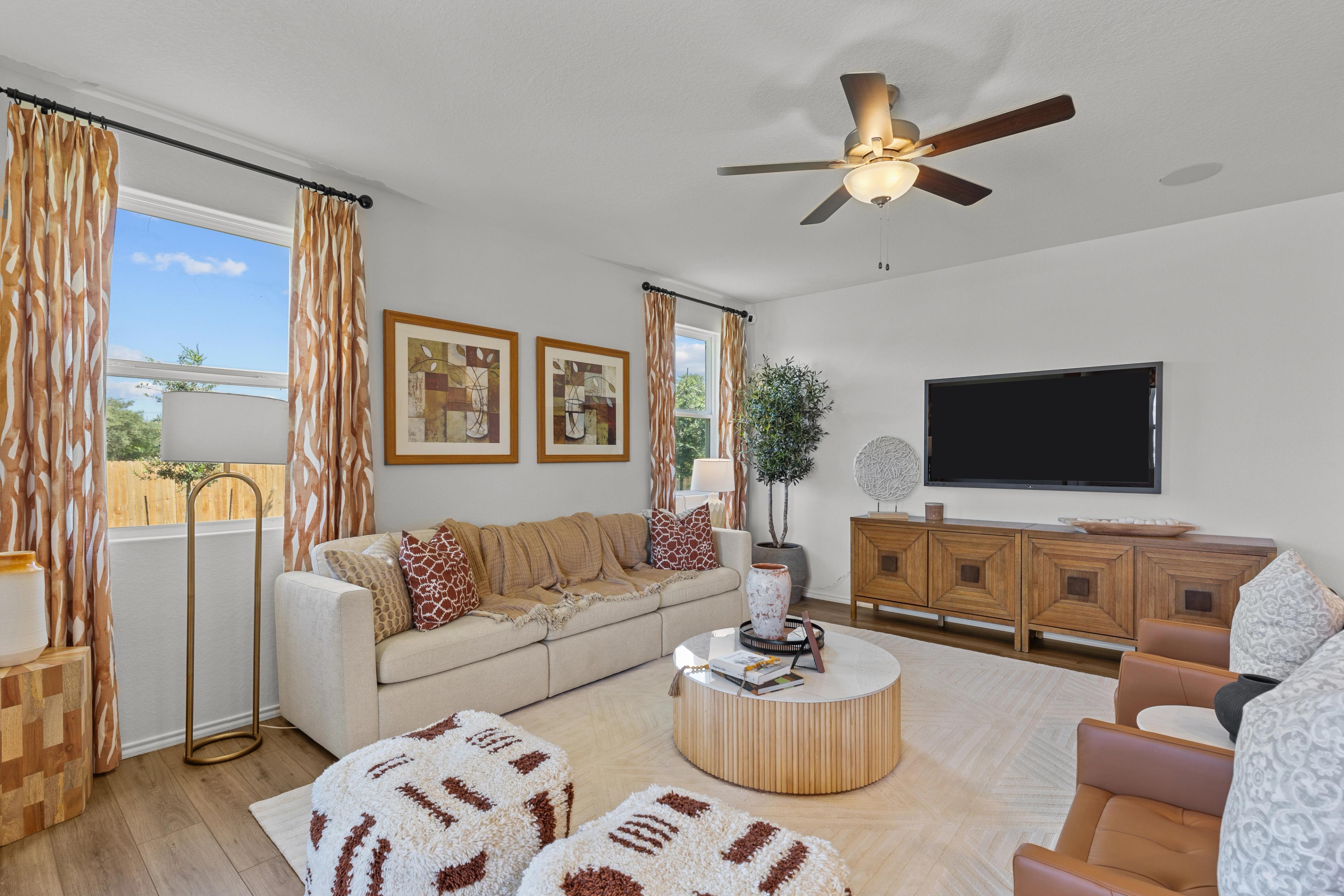 Cozy living room at Royal Crest in San Antonio Texas featuring beige sofa, wooden media console, TV, and large windows with patterned curtains