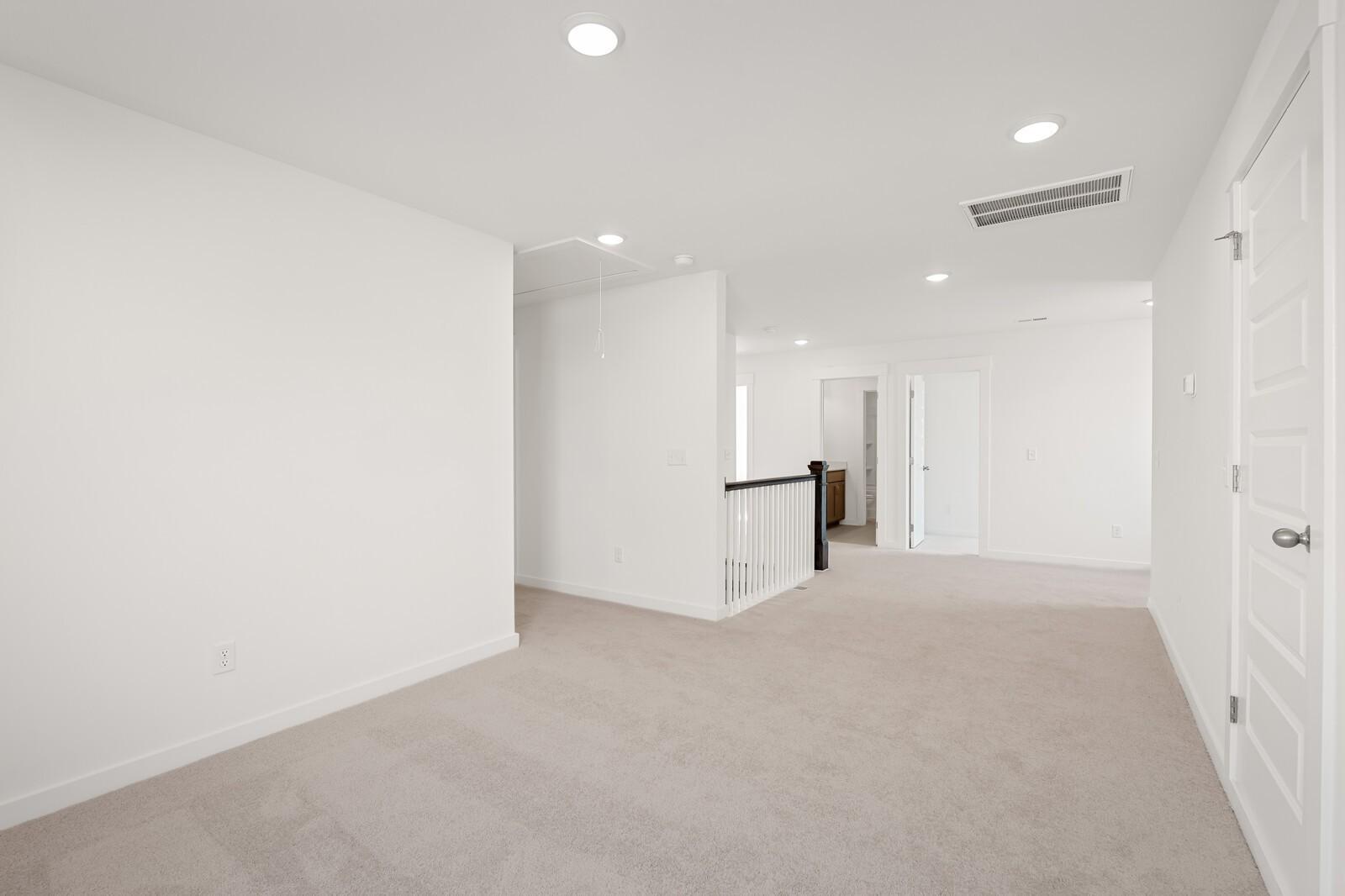 Spacious upstairs loft with white walls, beige carpet, recessed lights, and balcony railing in Davidson Homes The Ash C, Mt. Juliet