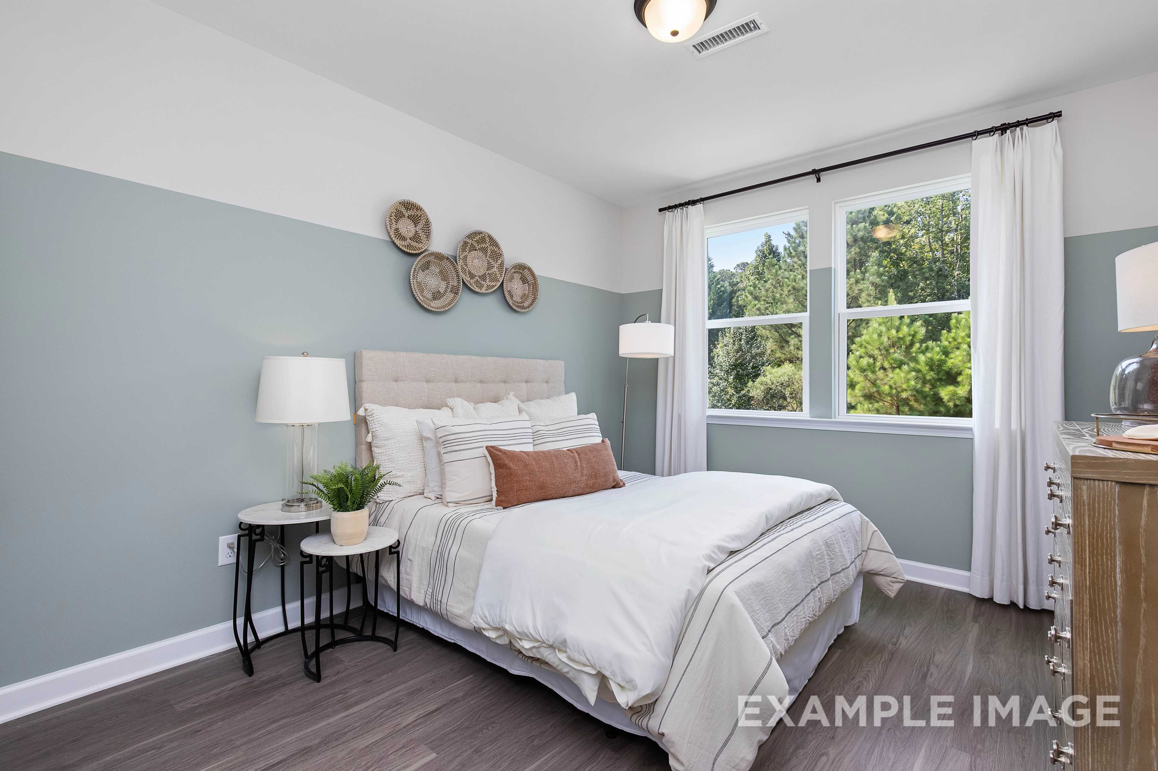 Serene master bedroom in The Willow B featuring white tufted bed, woven wall baskets, large window, and hardwood floors