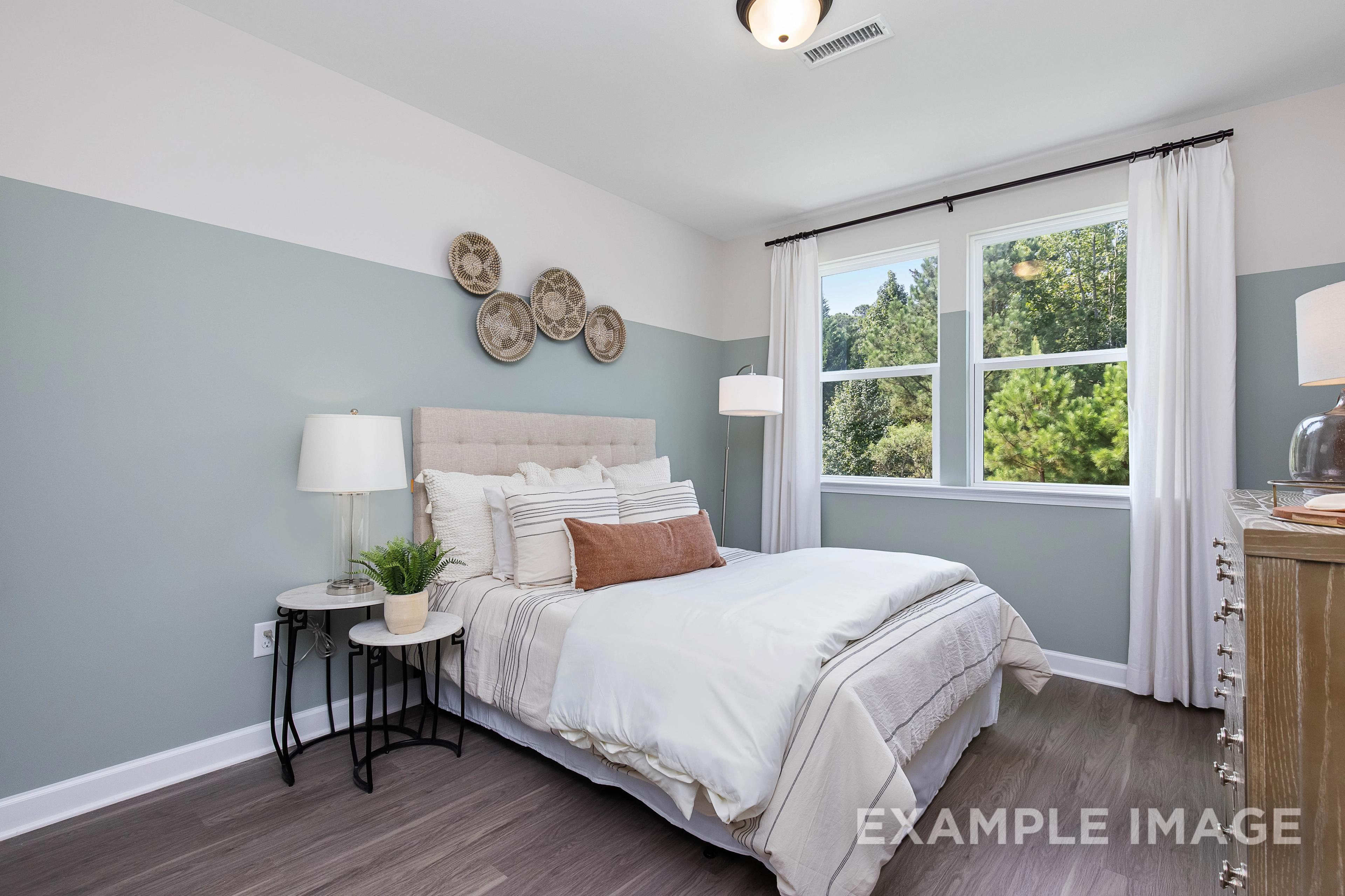Serene master bedroom in The Willow B featuring white tufted bed, woven wall baskets, large window, and hardwood floors