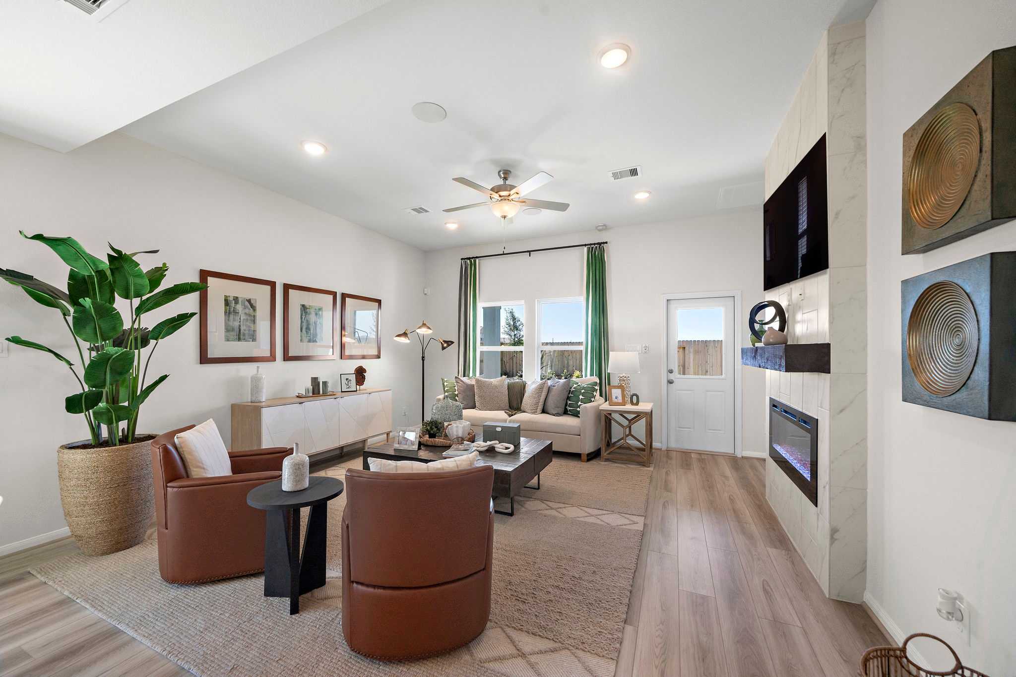 Open-concept living room at River Ranch Meadows in Dayton Texas featuring hardwood floors, gas fireplace, leather armchairs, and potted plants