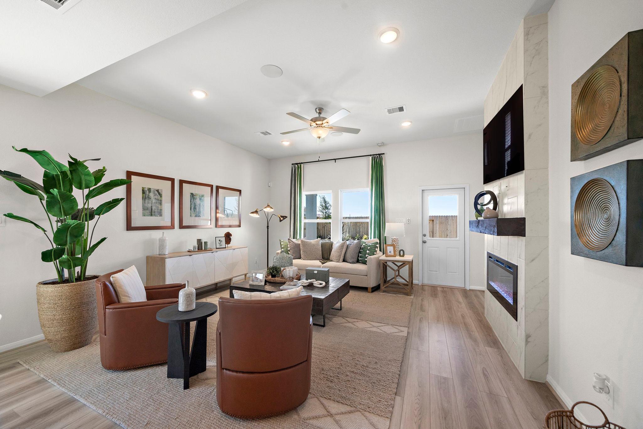 Open-concept living room at River Ranch Meadows in Dayton Texas featuring hardwood floors, gas fireplace, leather armchairs, and potted plants