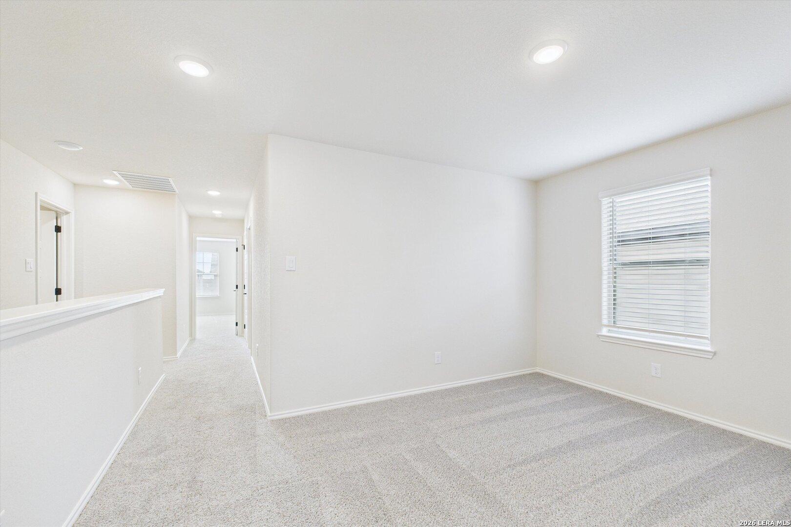 Bright upstairs hallway with white walls, carpeted floors, and bedroom doors in Davidson Homes The Gillian B, San Antonio, Texas