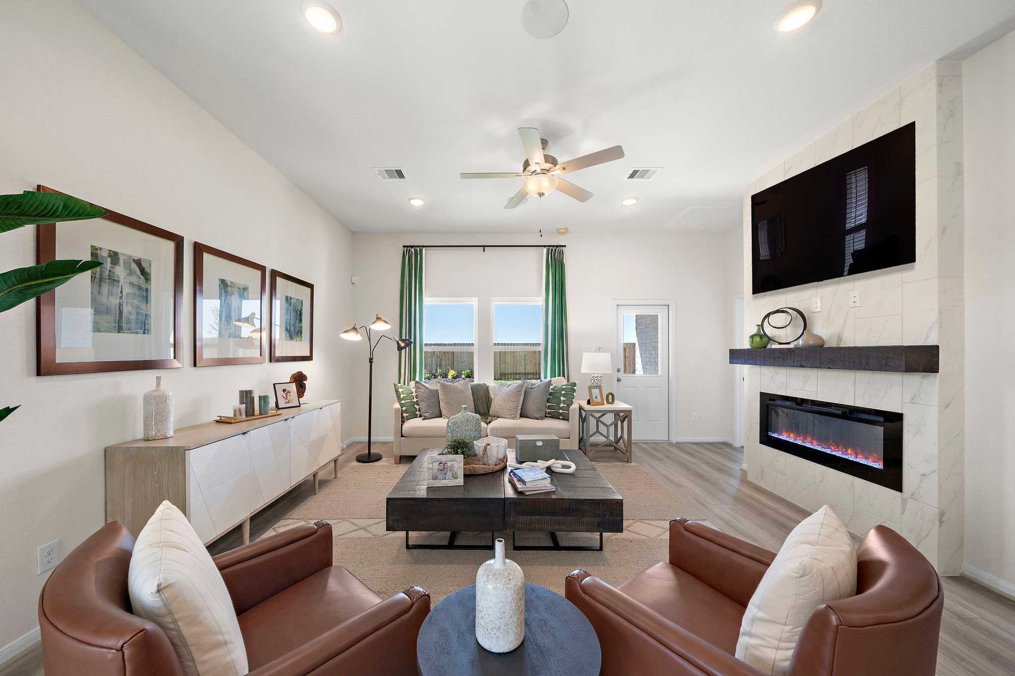 Spacious living room at River Ranch Meadows in Dayton TX with gray sofa, leather armchairs, electric fireplace, TV wall, and hardwood floors