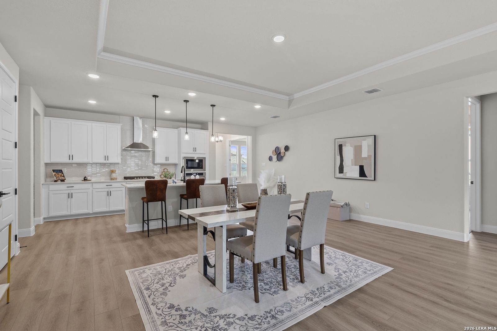 Modern open-concept kitchen with white cabinets, island bar stools, dining table, and hardwood floors in The Lanier G, Castroville, Texas