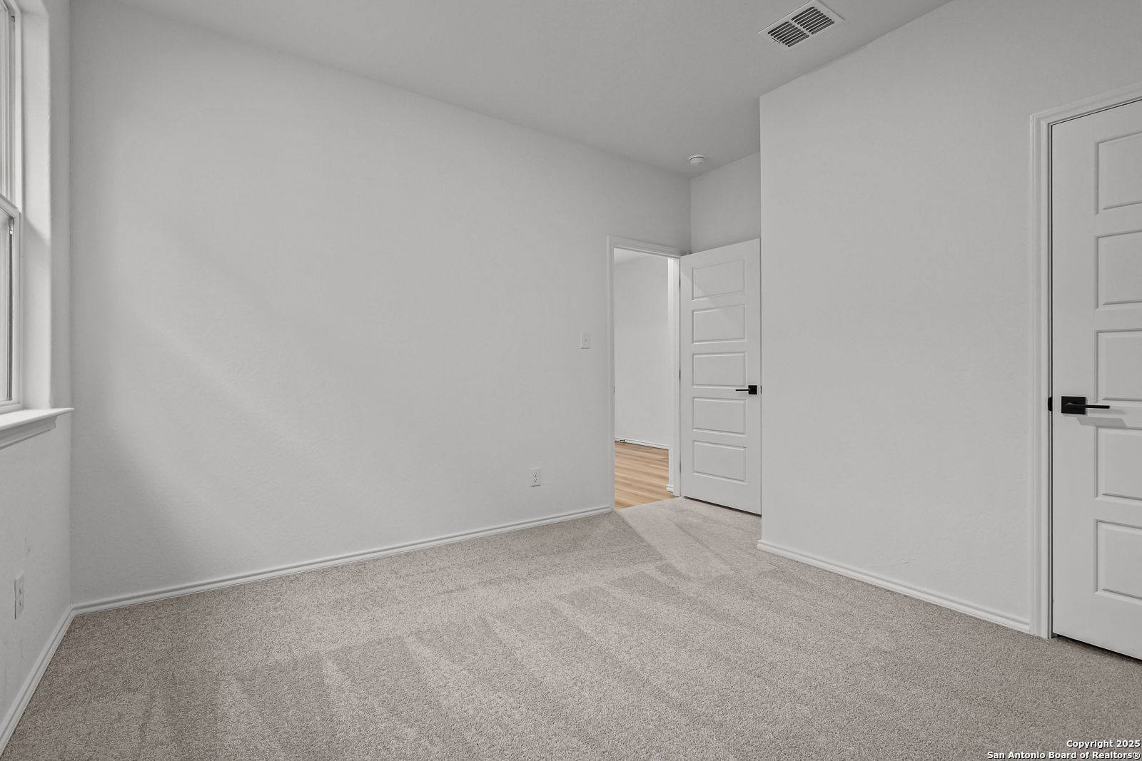 Spacious empty bedroom with beige carpet, white walls, and double doors in Davidson Homes The Daphne J, Converse, Texas