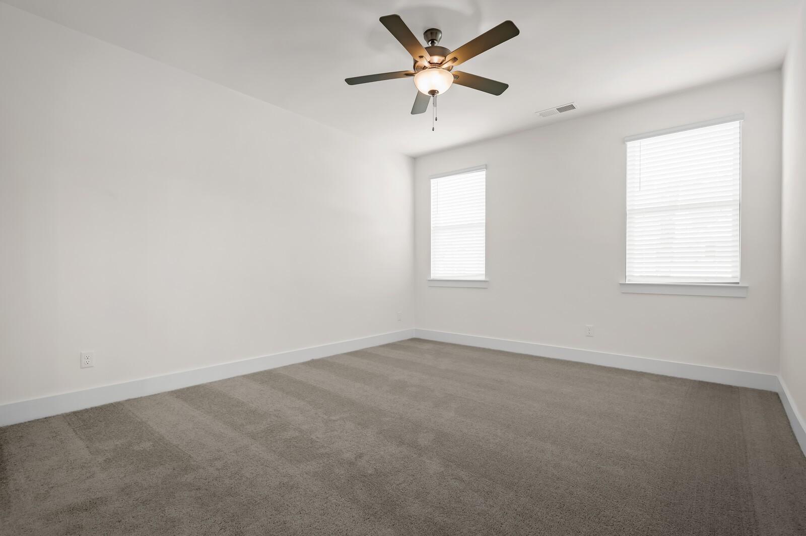 Spacious secondary bedroom with ceiling fan and plush carpeting in The Ash A floor plan at Woods Crossing, Gallatin, TN.