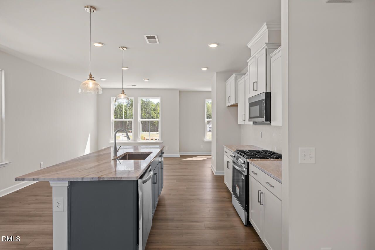 Open-concept kitchen with white cabinets, island sink, and gas range in Davidson Homes The Mitchell plan, Knightdale, NC