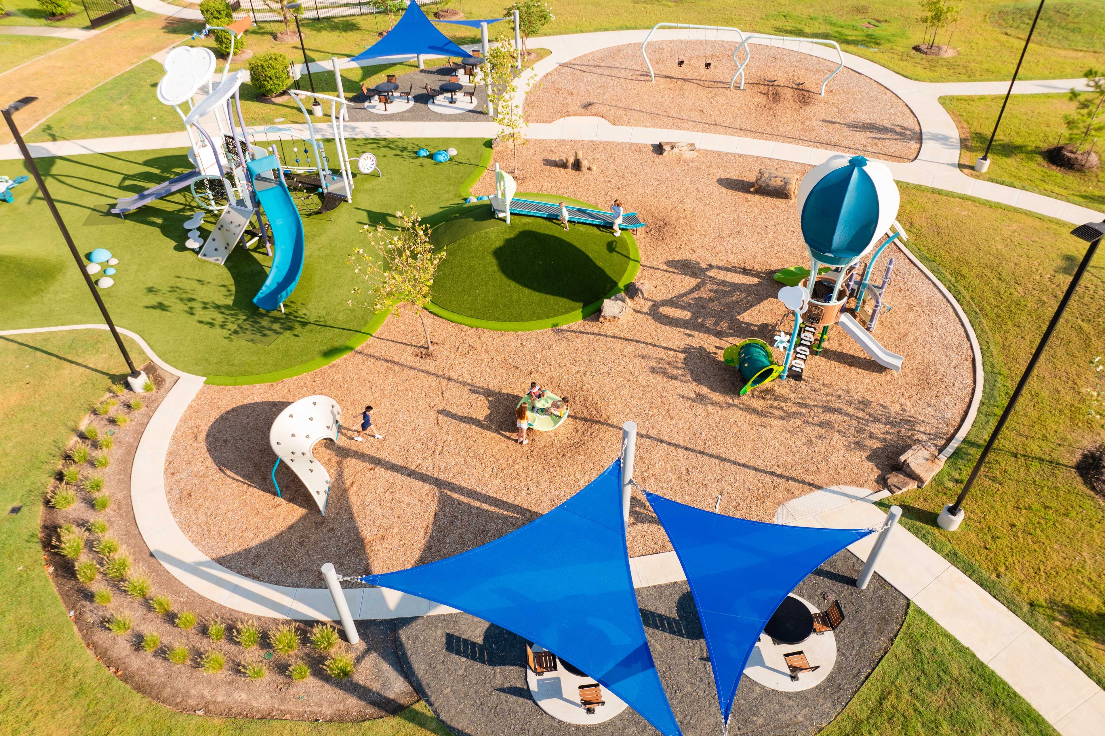 Children's playground at Sunterra in Katy Texas featuring blue slides, climbing structures, and shaded canopies