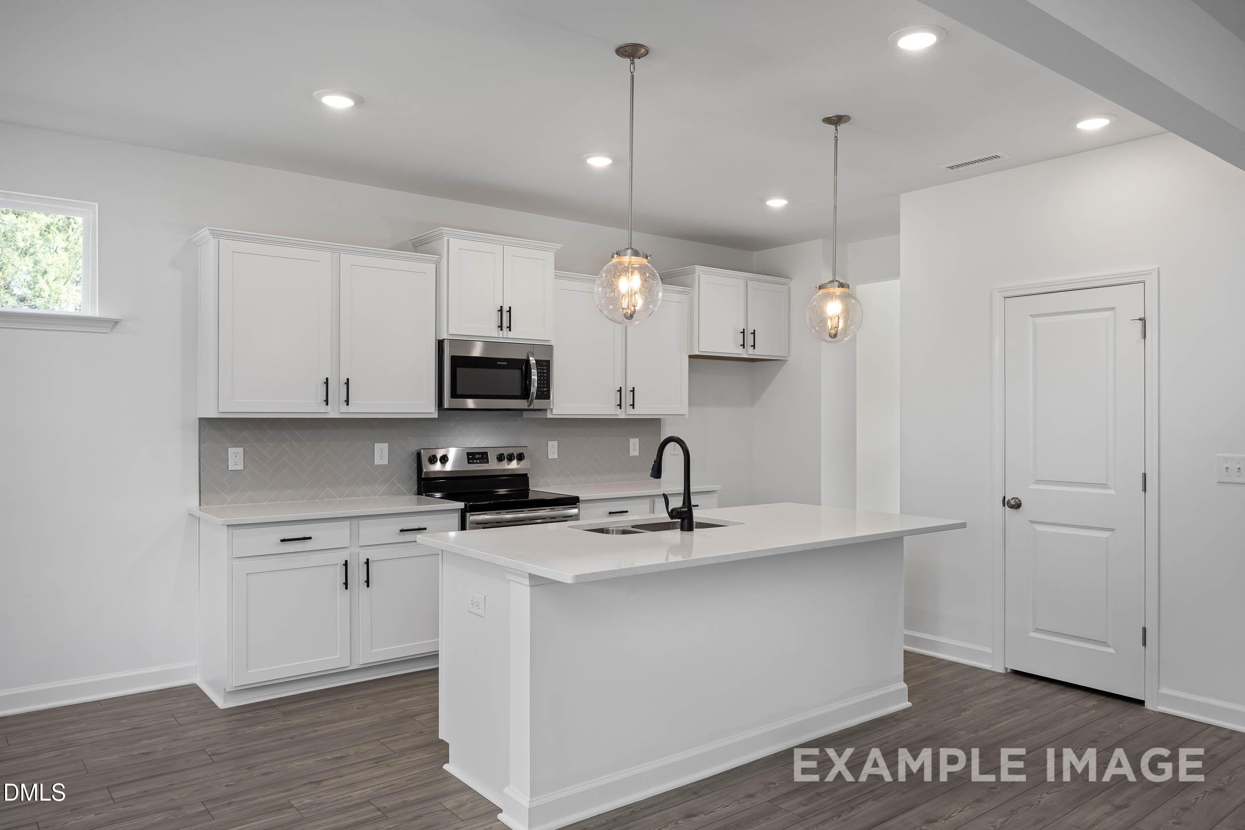 Bright modern kitchen with white shaker cabinets, quartz island sink, stainless appliances, and pendant lights in Davidson Homes The Willow D, Zebulon, NC