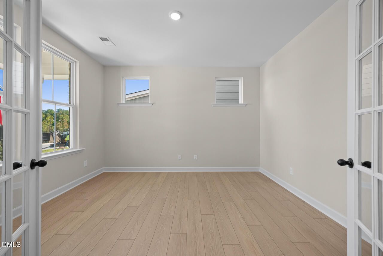 Bright empty room with luxury vinyl plank flooring and French doors in Davidson Homes Ashport M plan, Wendell Ridge, NC
