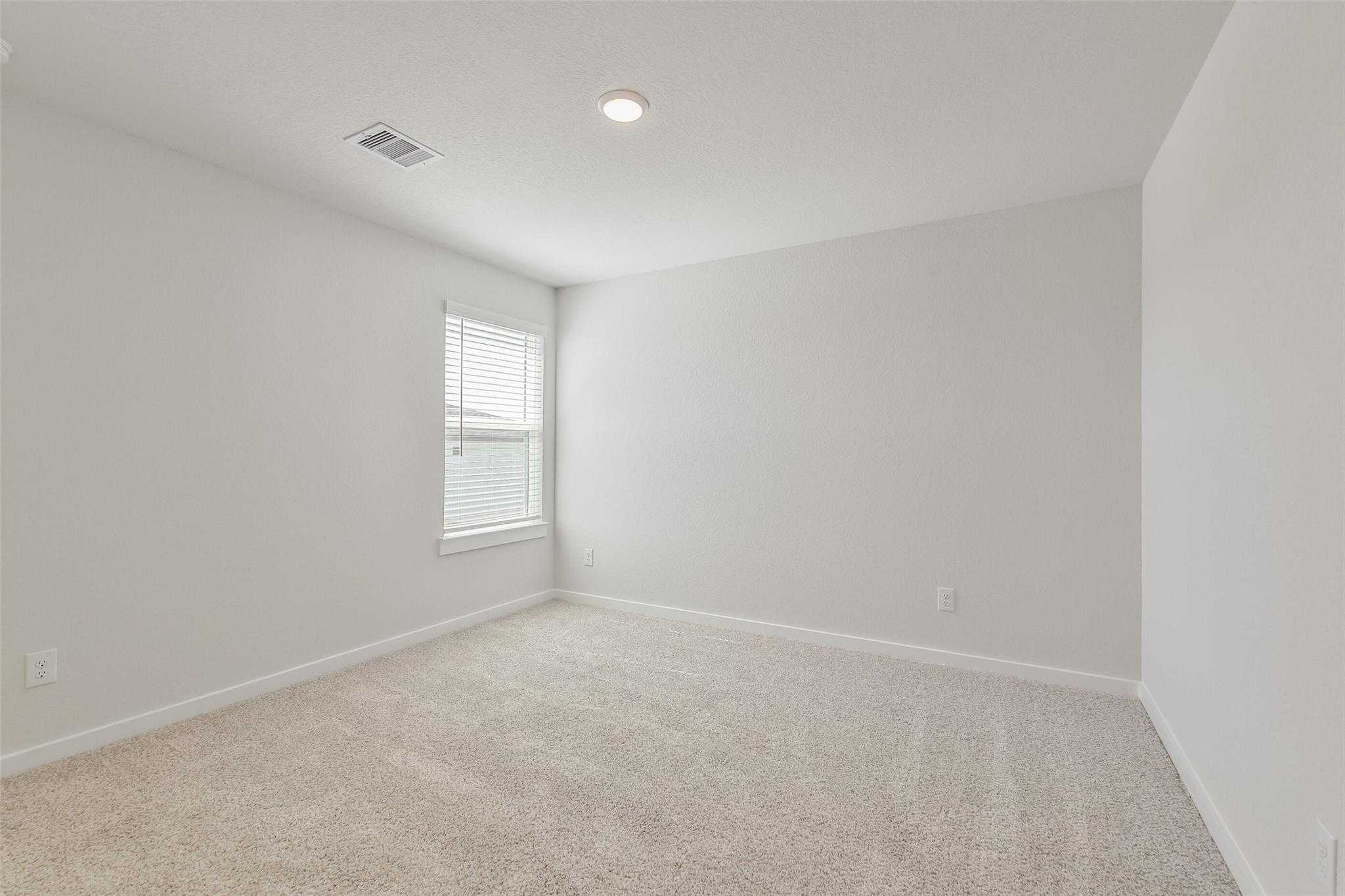 Bright empty bedroom with light gray walls, beige carpet, and window blinds in Davidson Homes The Rio Grande H, Magnolia, Texas