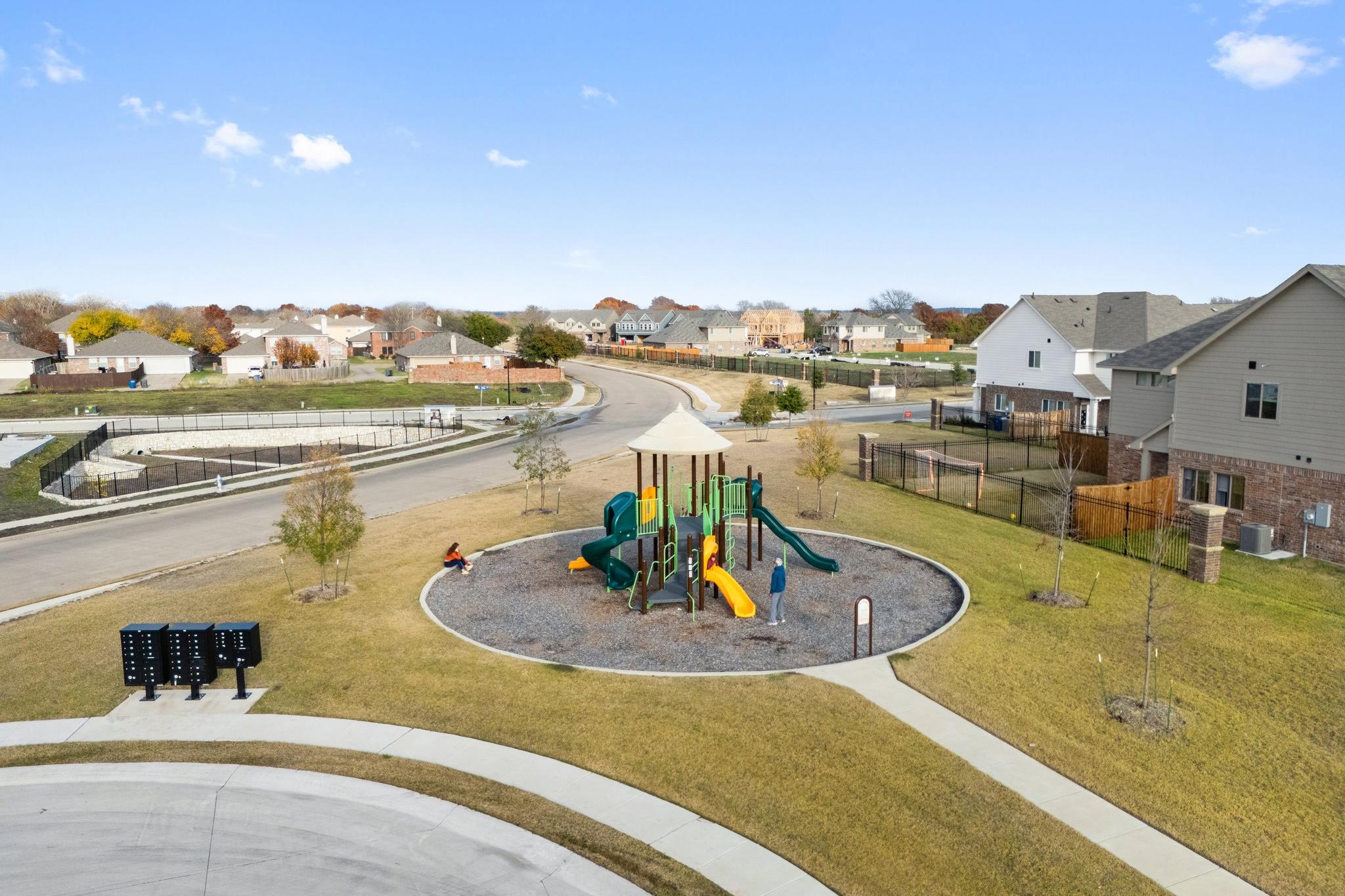 Children's playground at Lake Park Villas in Wylie TX with colorful slides, swings, rubber surfacing, and nearby suburban homes