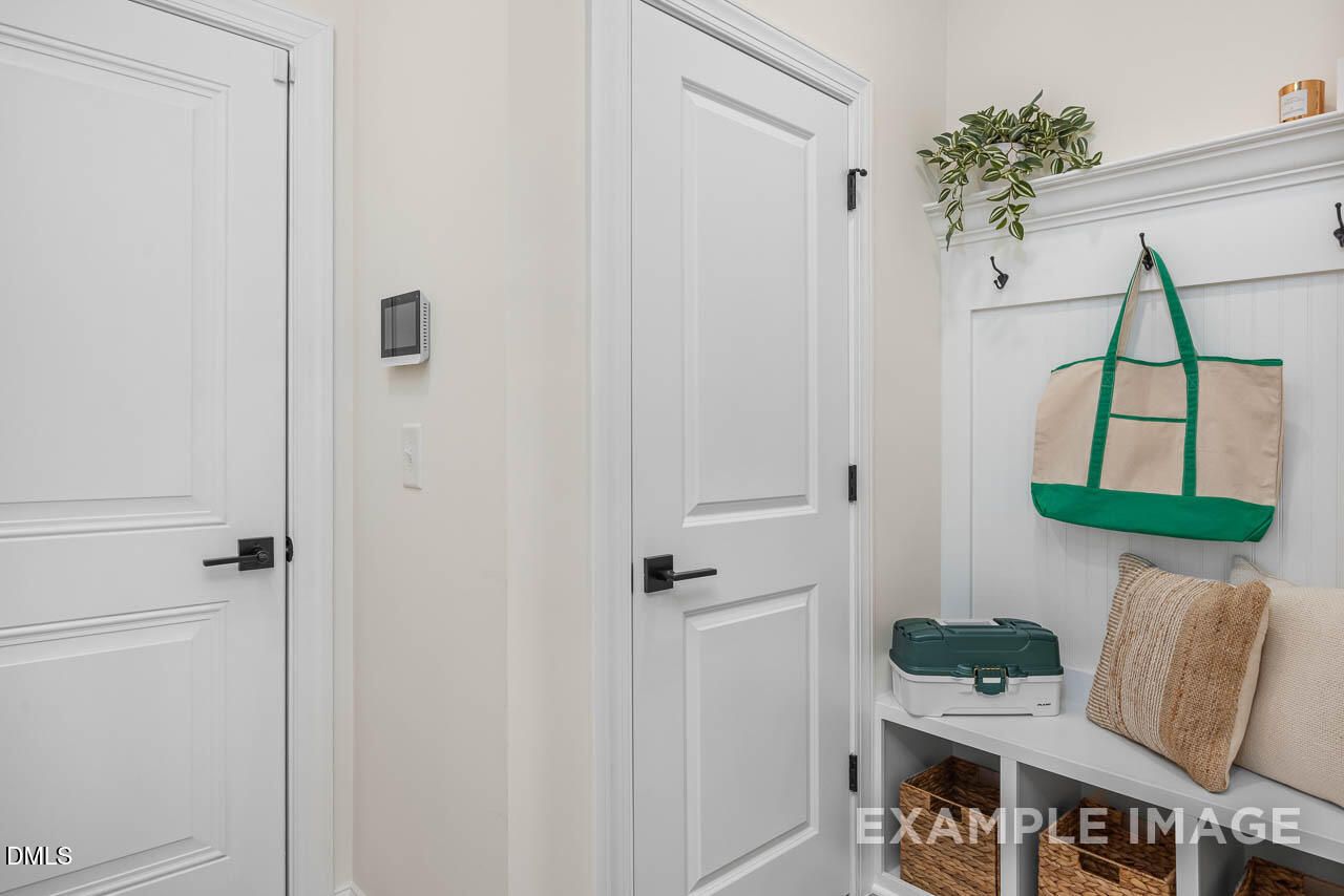 Functional mudroom with white doors, built-in bench, wicker storage baskets, and coat hooks in Davidson Homes The Crawford D, Angier, NC
