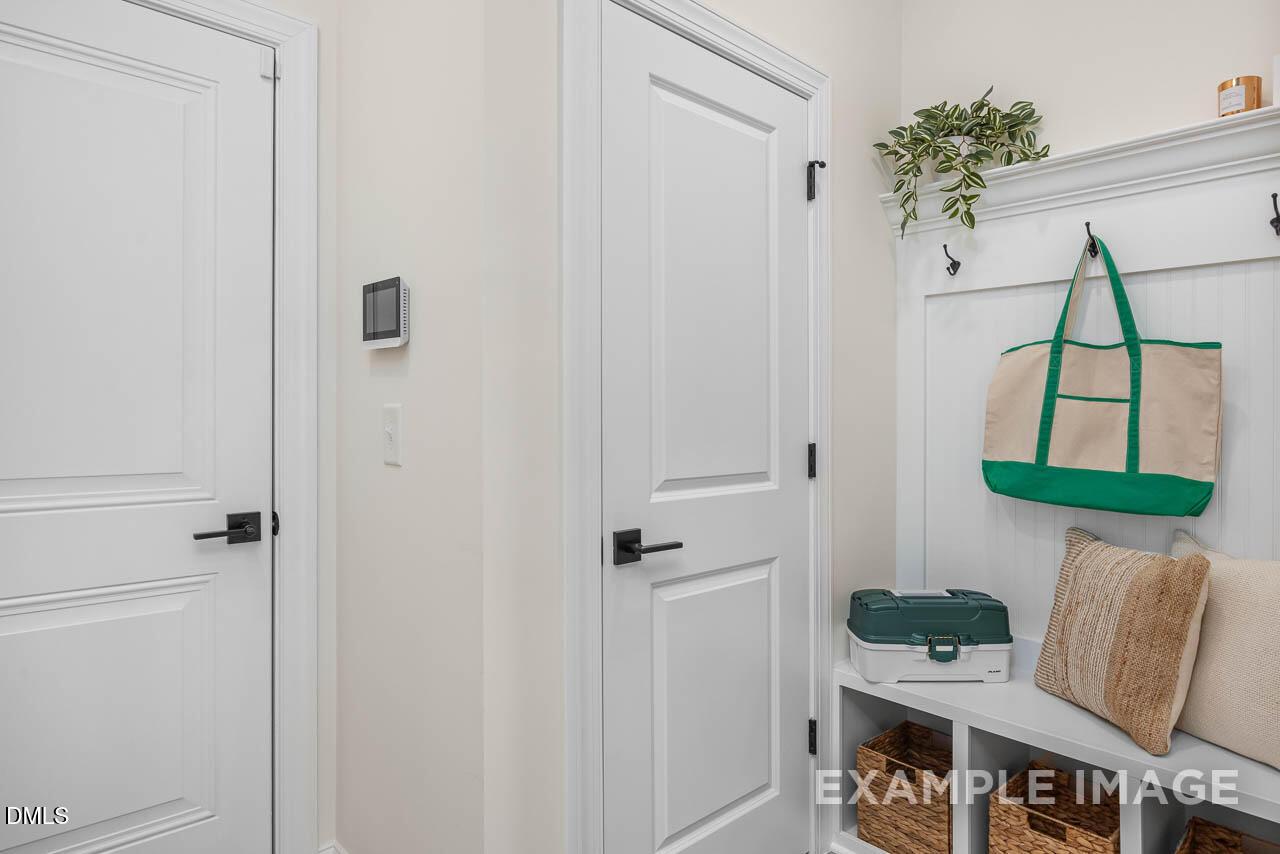 Functional mudroom with white doors, built-in bench, wicker storage baskets, and coat hooks in Davidson Homes The Crawford D, Angier, NC