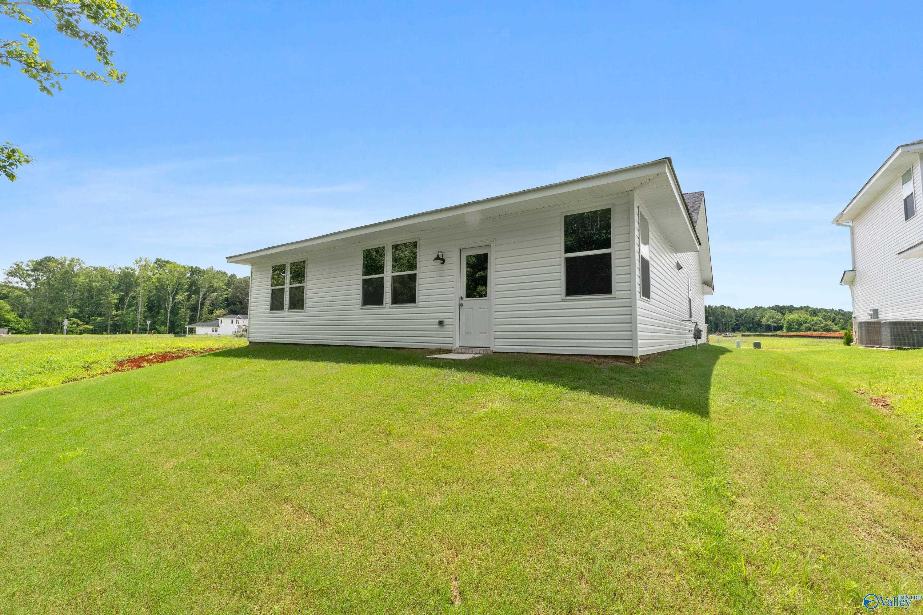White single-story home exterior with 2-car garage, large windows, lush green lawn, and blue sky in Forest Glen, Hazel Green, Alabama