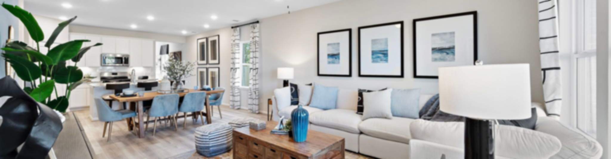 Spacious open-concept living and dining area in new Heartland home, white sofas, wooden table, blue chairs, modern art