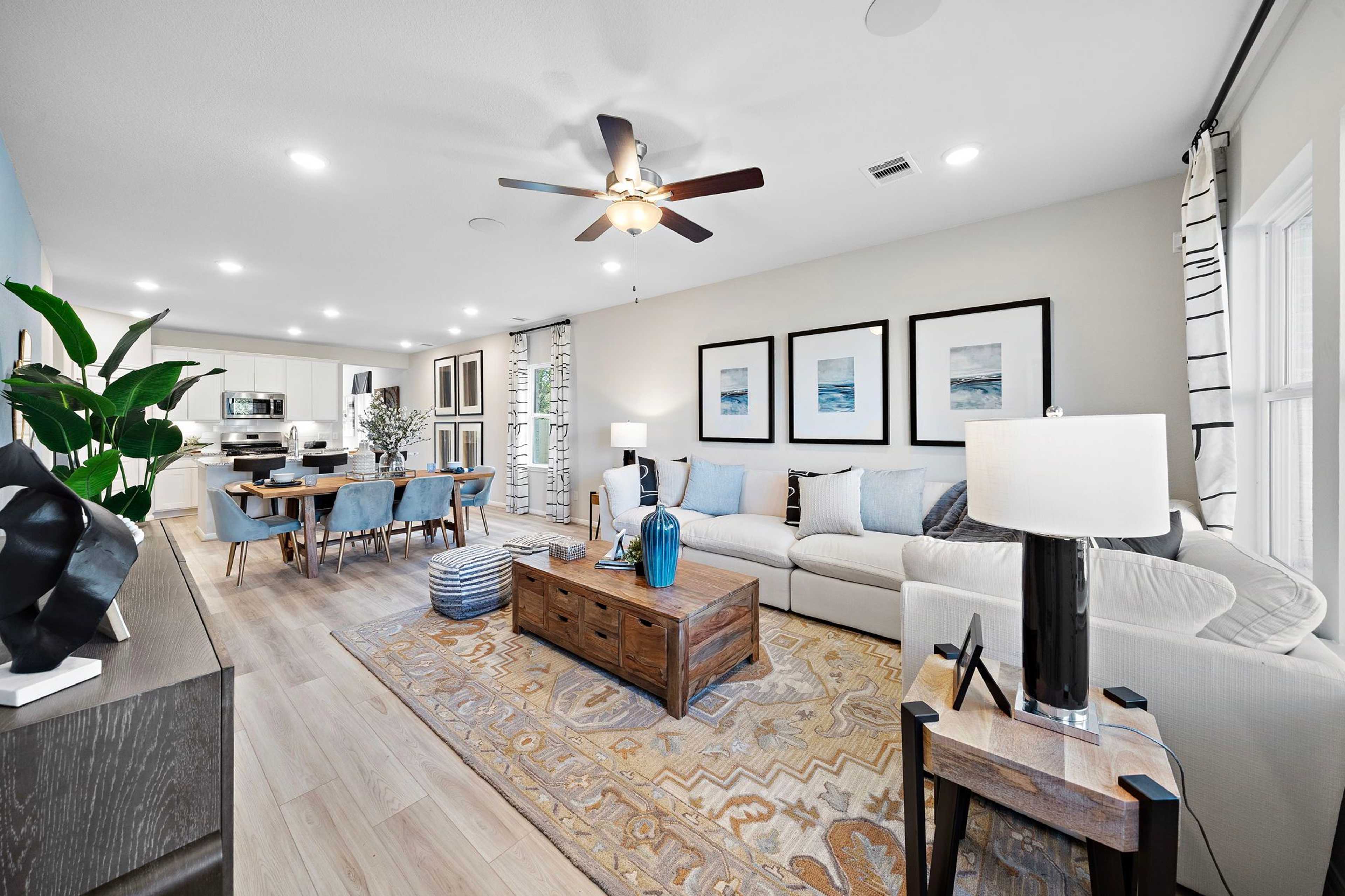 Open-concept living and dining room in Heartland Texas Davidson Homes with hardwood floors, white sofa, blue accents, and wall art