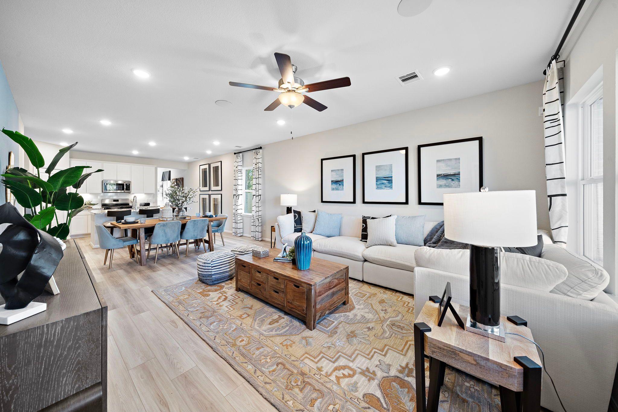 Open-concept living and dining room in Heartland Texas Davidson Homes with hardwood floors, white sofa, blue accents, and wall art