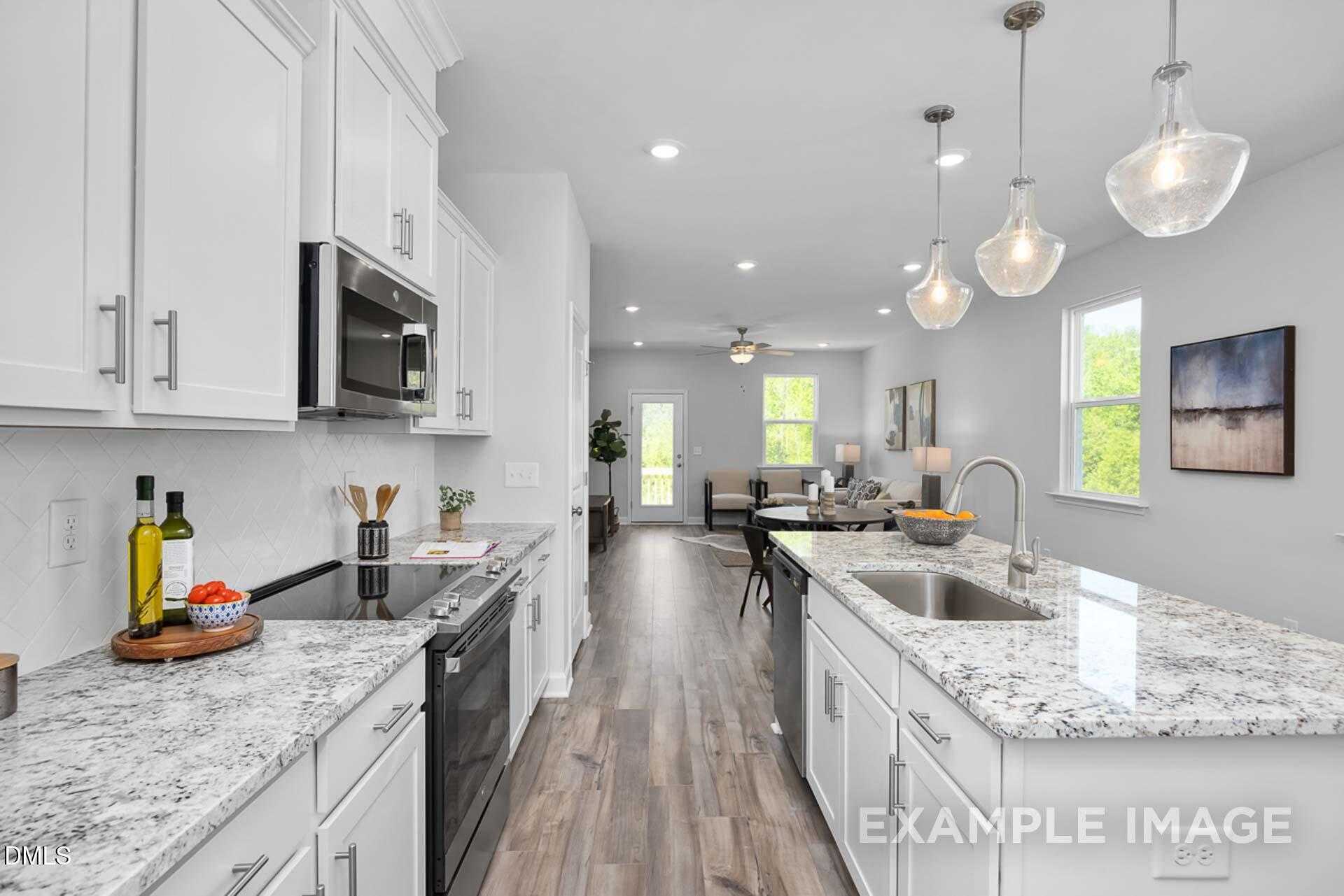 Modern open-concept kitchen with white shaker cabinets, quartz countertops, stainless appliances, and island sink in The Carter C 3-bedroom home, Lillington, NC