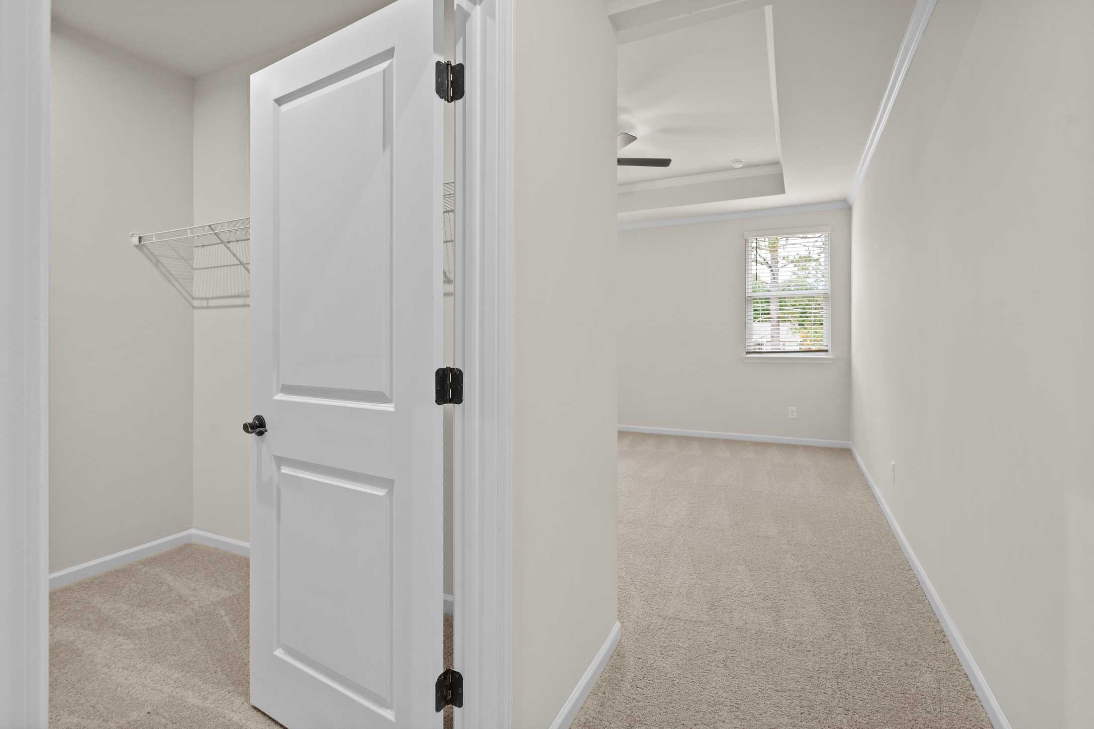 Spacious walk-in closet in The Glenwood B home featuring open white door, wire shelving, beige walls, carpet flooring, and bedroom window