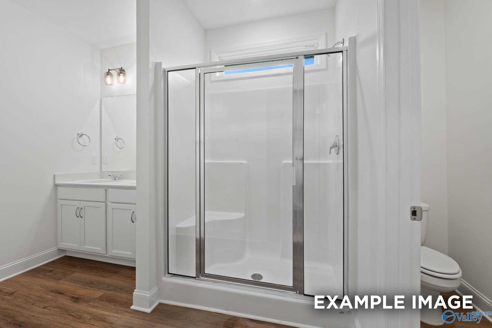 Modern frameless glass shower and white vanity in master bathroom of 4-bedroom The Daphne D home, Davidson Homes, Athens Alabama