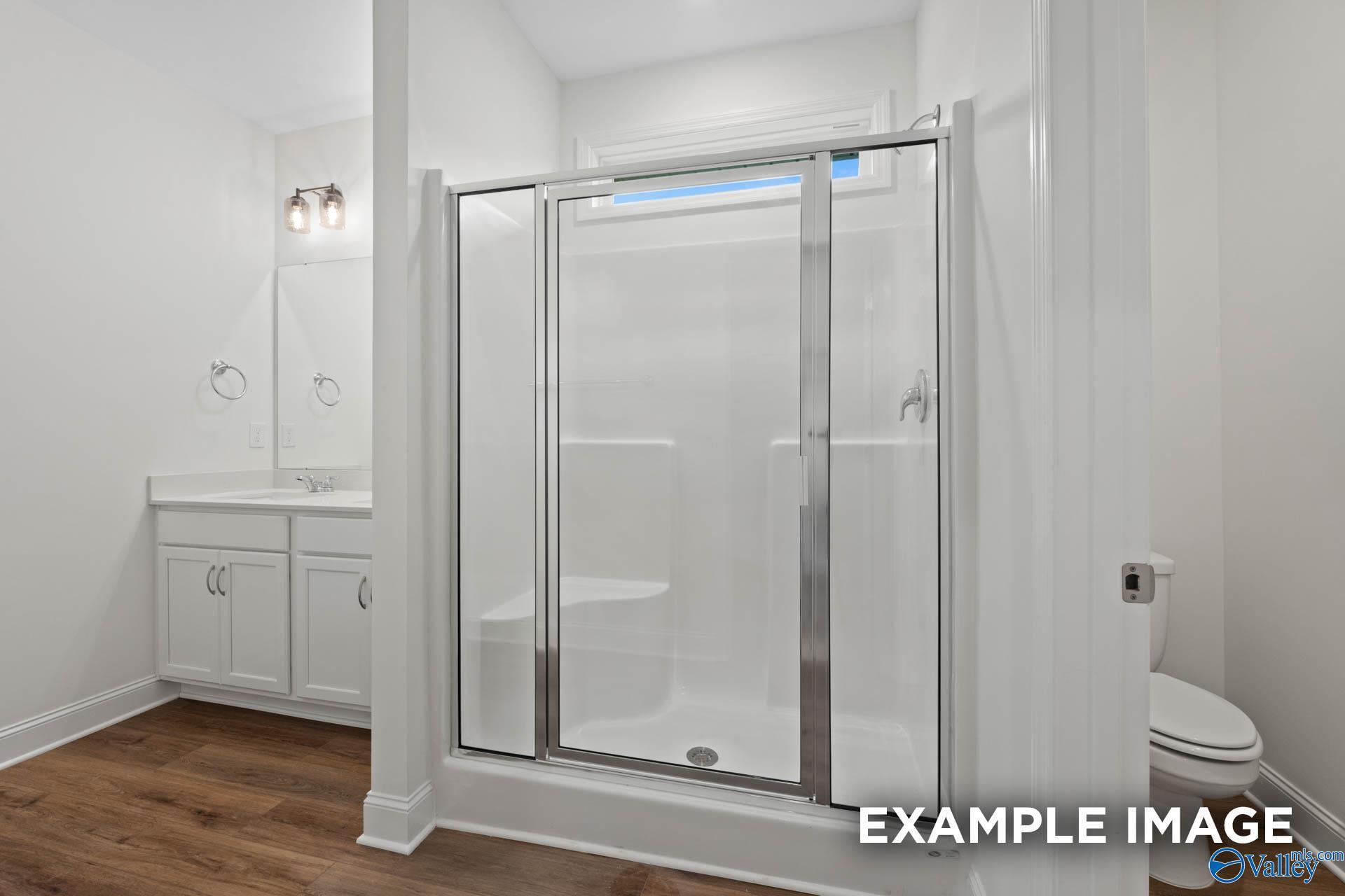 Modern white bathroom featuring glass shower enclosure, vanity sink, and toilet in Evermore Homes The Daphne E, Harvest, Alabama