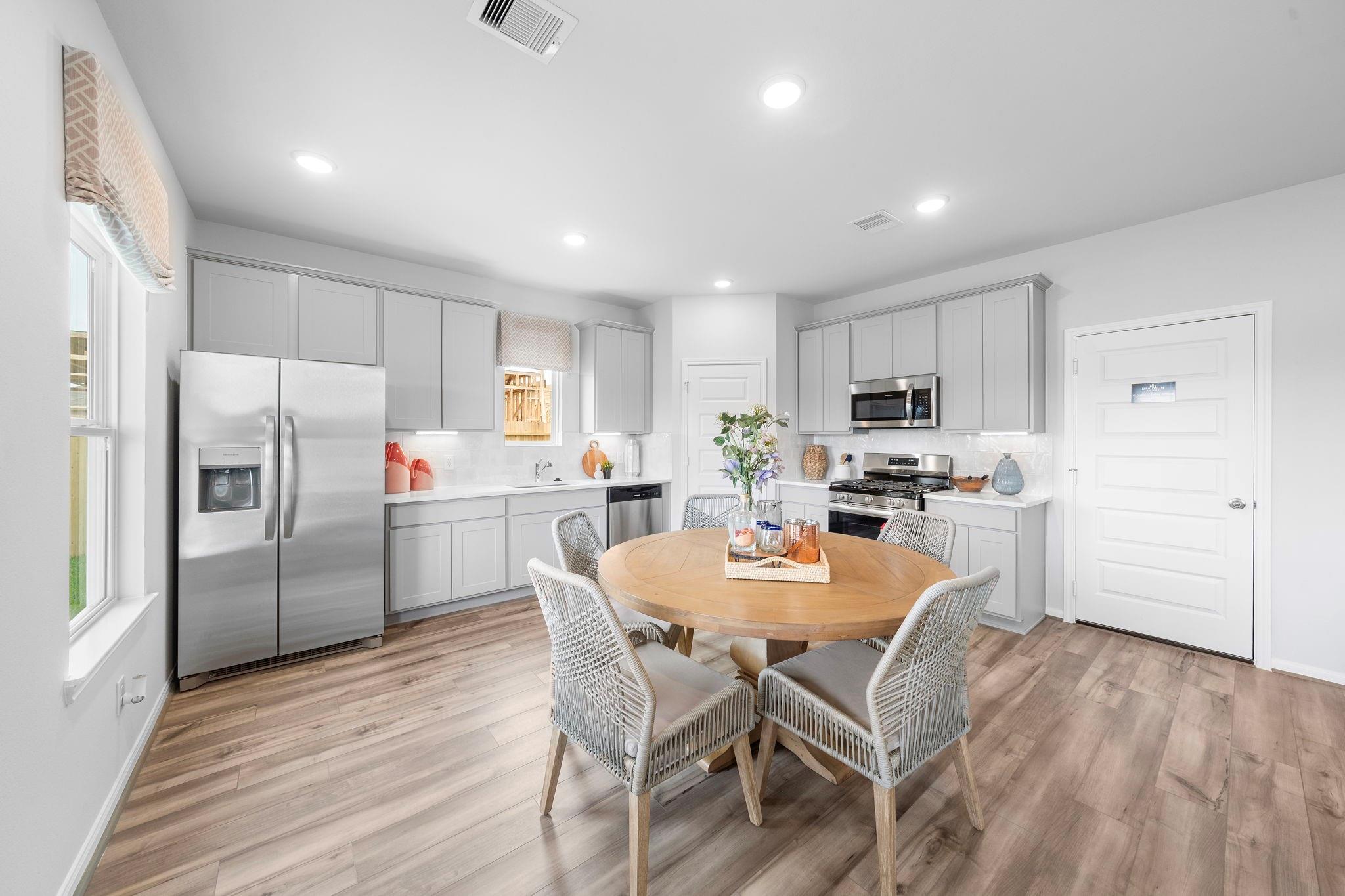 Bright kitchen with gray cabinets, stainless appliances, round wood dining table, and vinyl flooring in Davidson Homes Trinity F plan, Splendora, TX