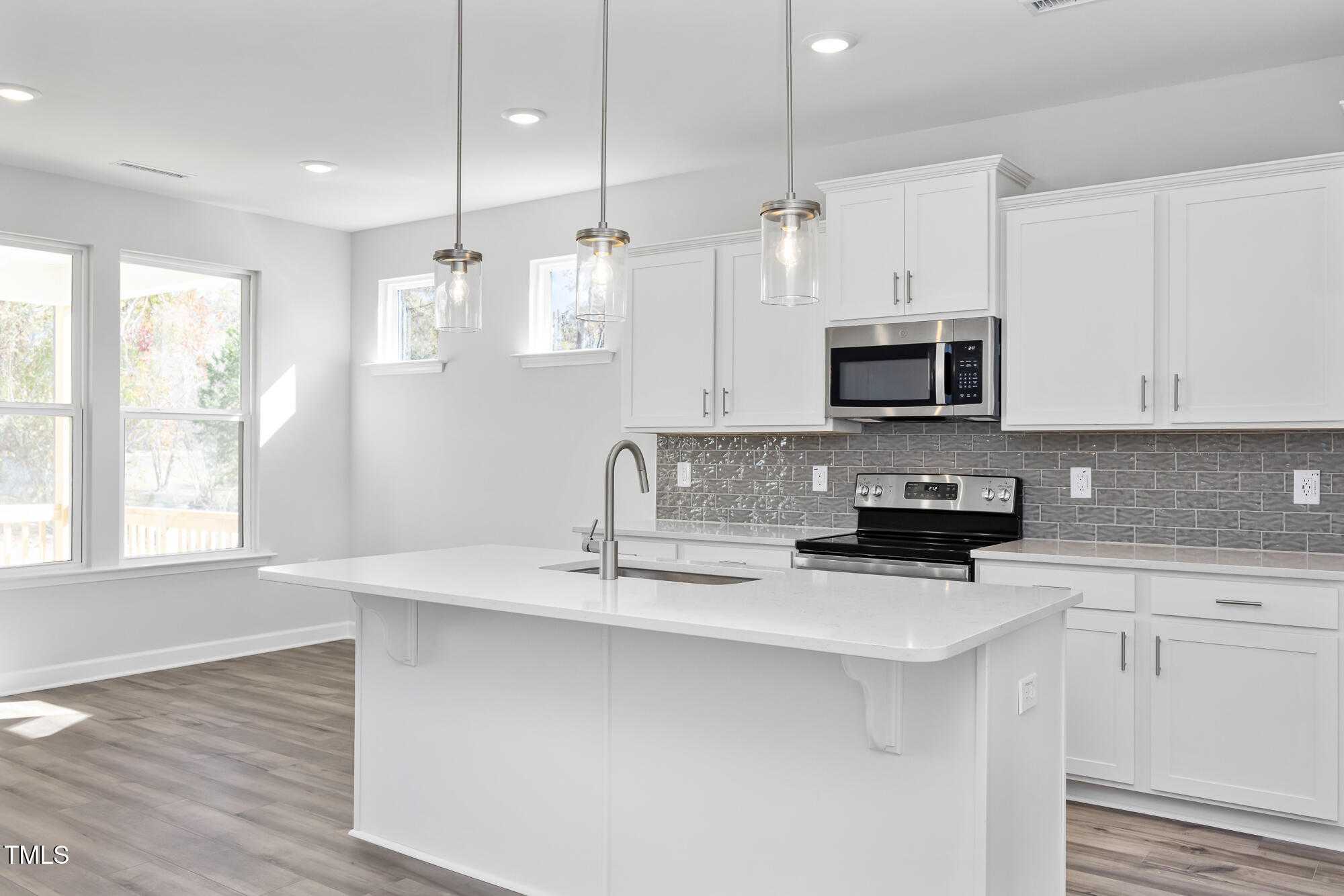 Bright modern kitchen with white cabinets, large island sink, stainless steel appliances, subway tile backsplash in Willow C home, Angier NC