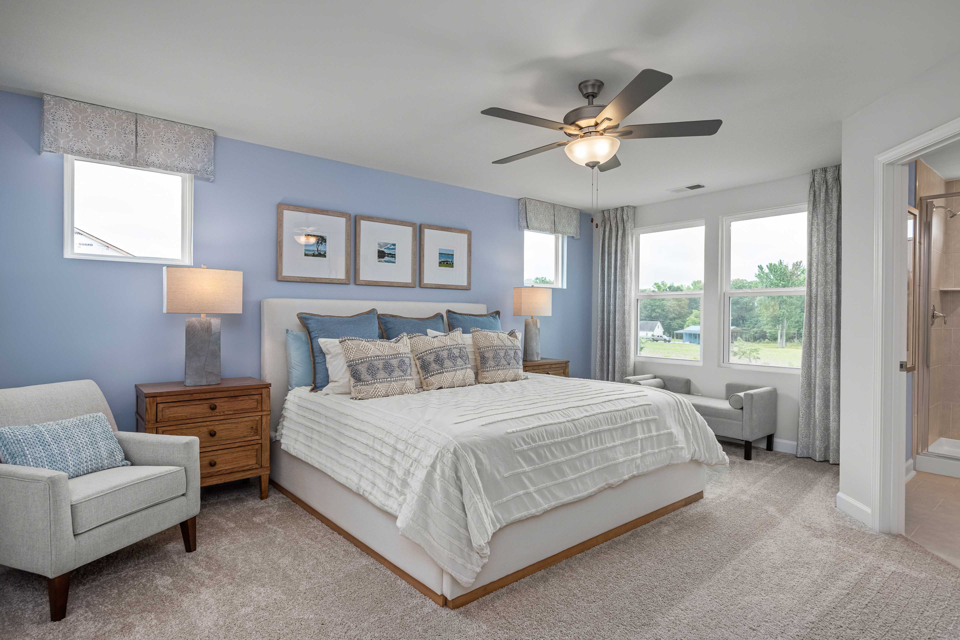 Spacious primary bedroom in Springvale Fuquay-Varina NC with blue walls king bed ceiling fan and large windows by Davidson Homes