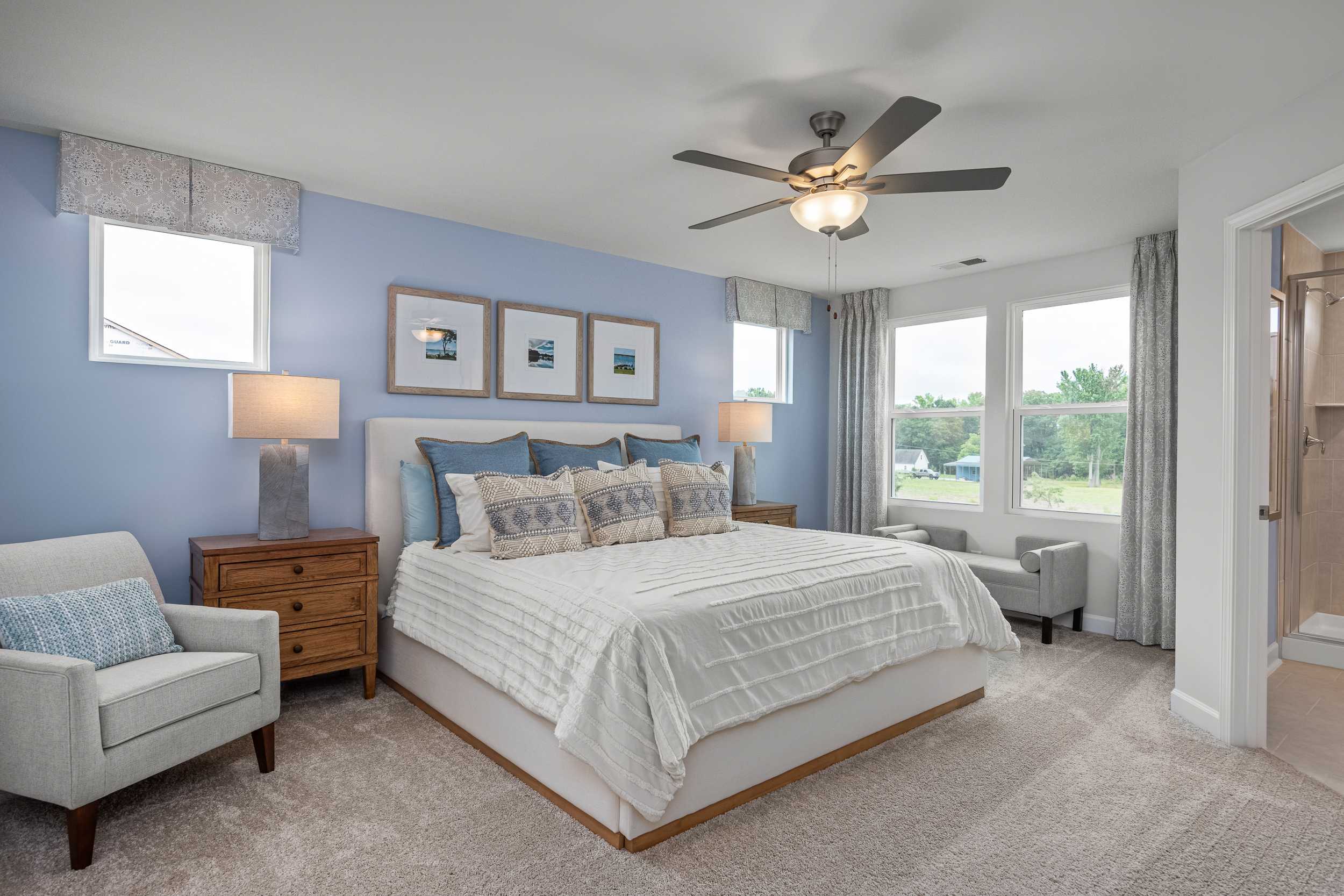 Spacious primary bedroom in Springvale Fuquay-Varina NC with blue walls king bed ceiling fan and large windows by Davidson Homes